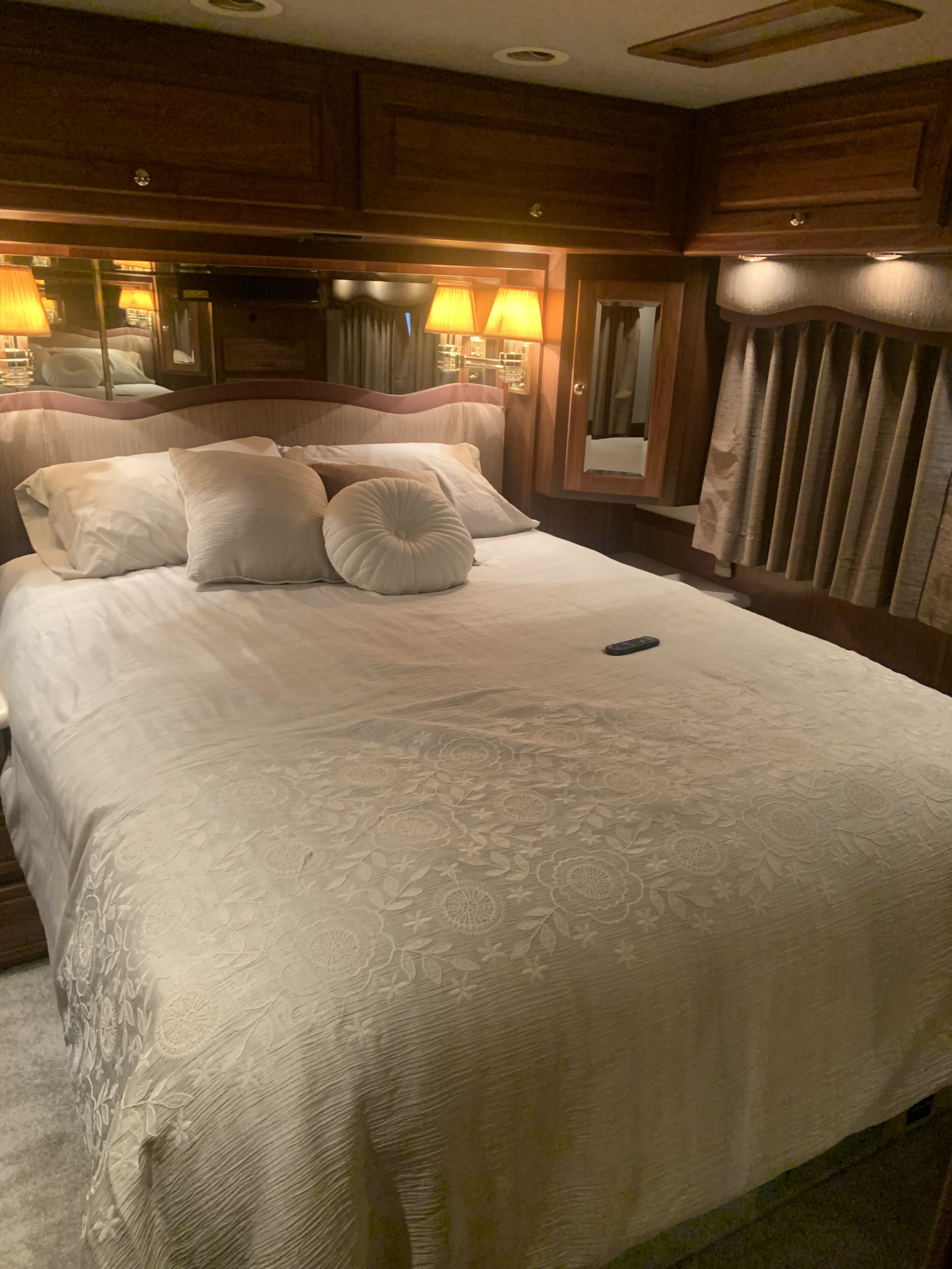 Cozy RV rental bedroom: large bed, plush pillows, intricate bedding, wood paneling, mirrors, and soft lighting for comfort.. Foretravel Unicoach 2000
