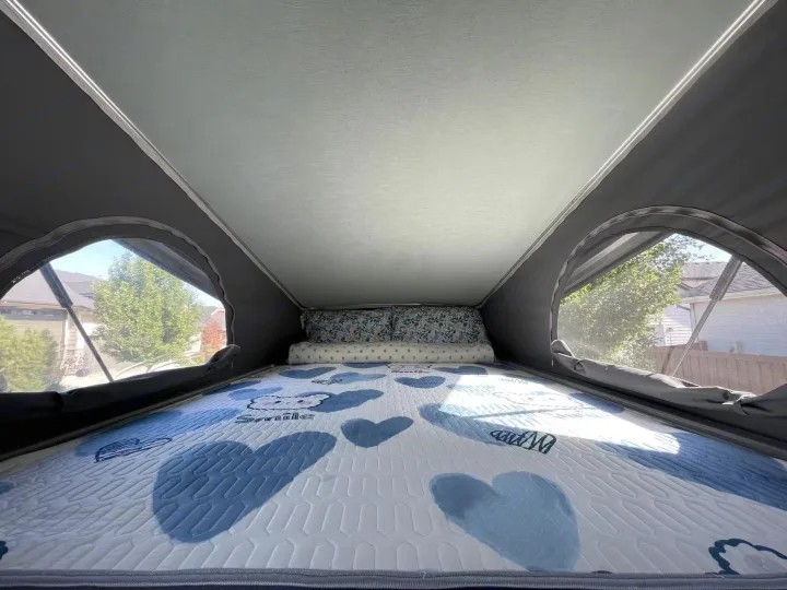 RV rental pop-top interior showing a bed with blue heart mattress and pillows. Mesh windows offer views of trees and houses.. Winnebago Solis Pocket 2022