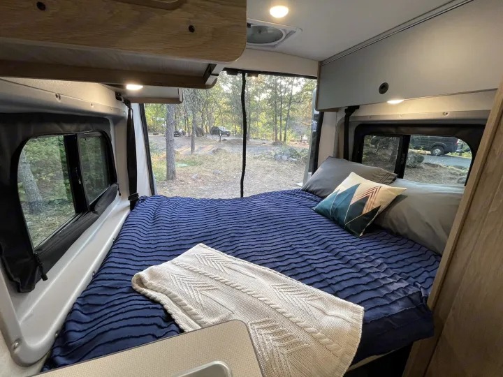 Cozy RV rental bedroom with a comfy bed, pillows, and a scenic view of the woods for your next camping adventure.. Winnebago Solis Pocket 2022