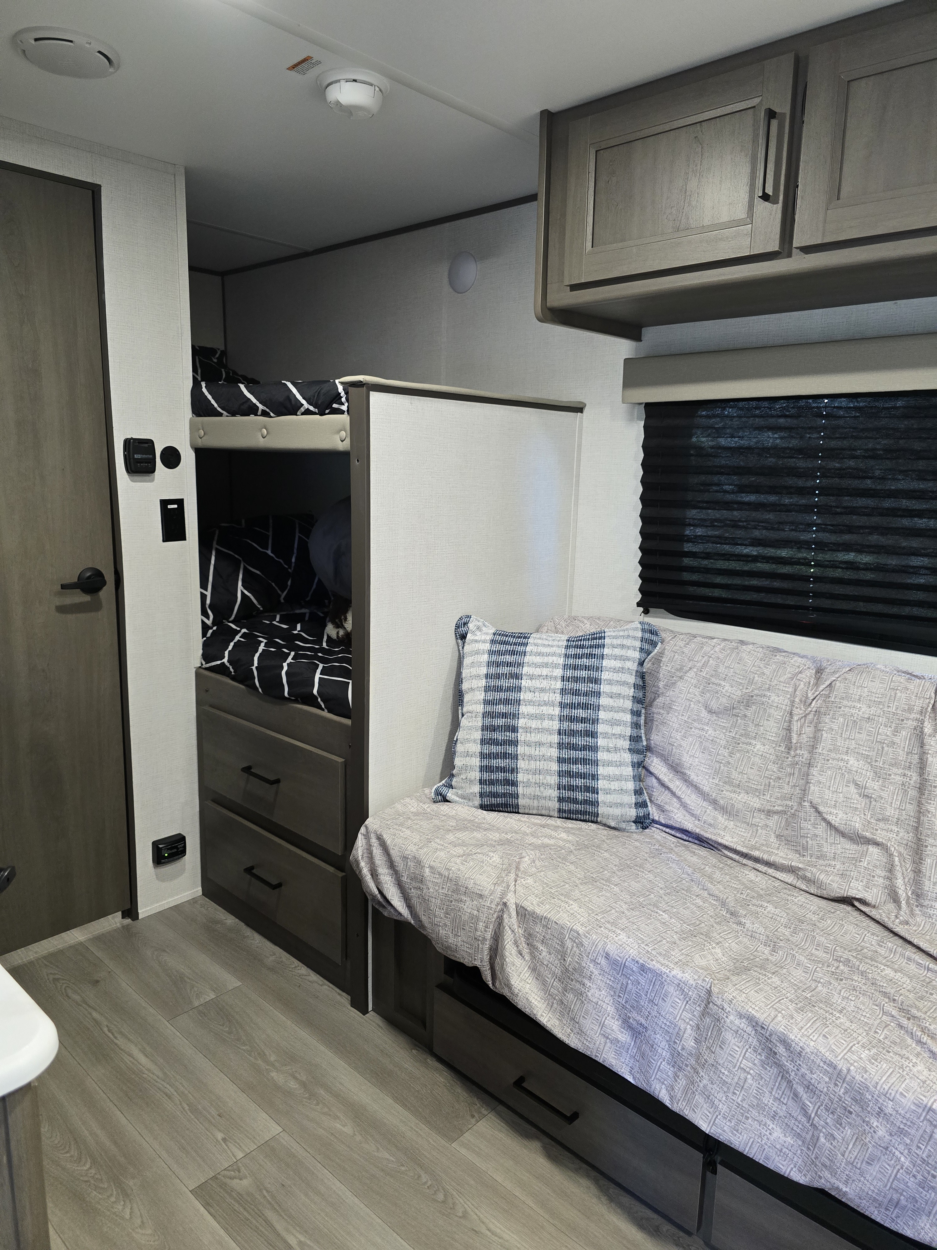 Cozy RV rental interior with bunk beds, a comfy sofa/dinette, overhead cabinets, and durable wood-look flooring.. Grand Design 151BH 2025