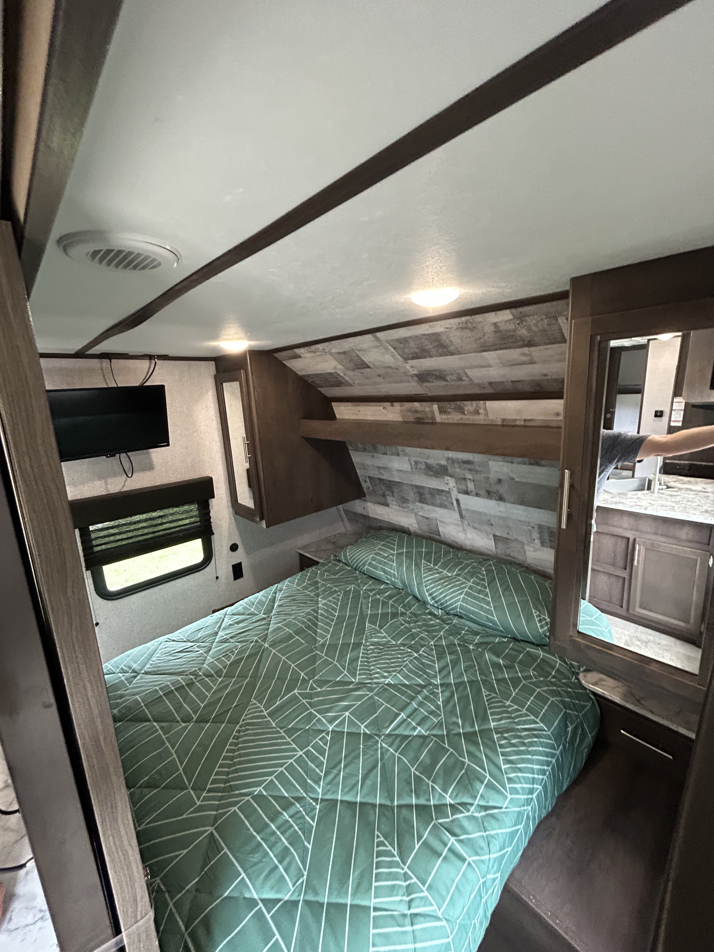 Step into comfort! This RV rental bedroom features a green patterned bed, wall-mounted TV, window, and mirrored storage.. Dutchmen Coleman Lantern 2020
