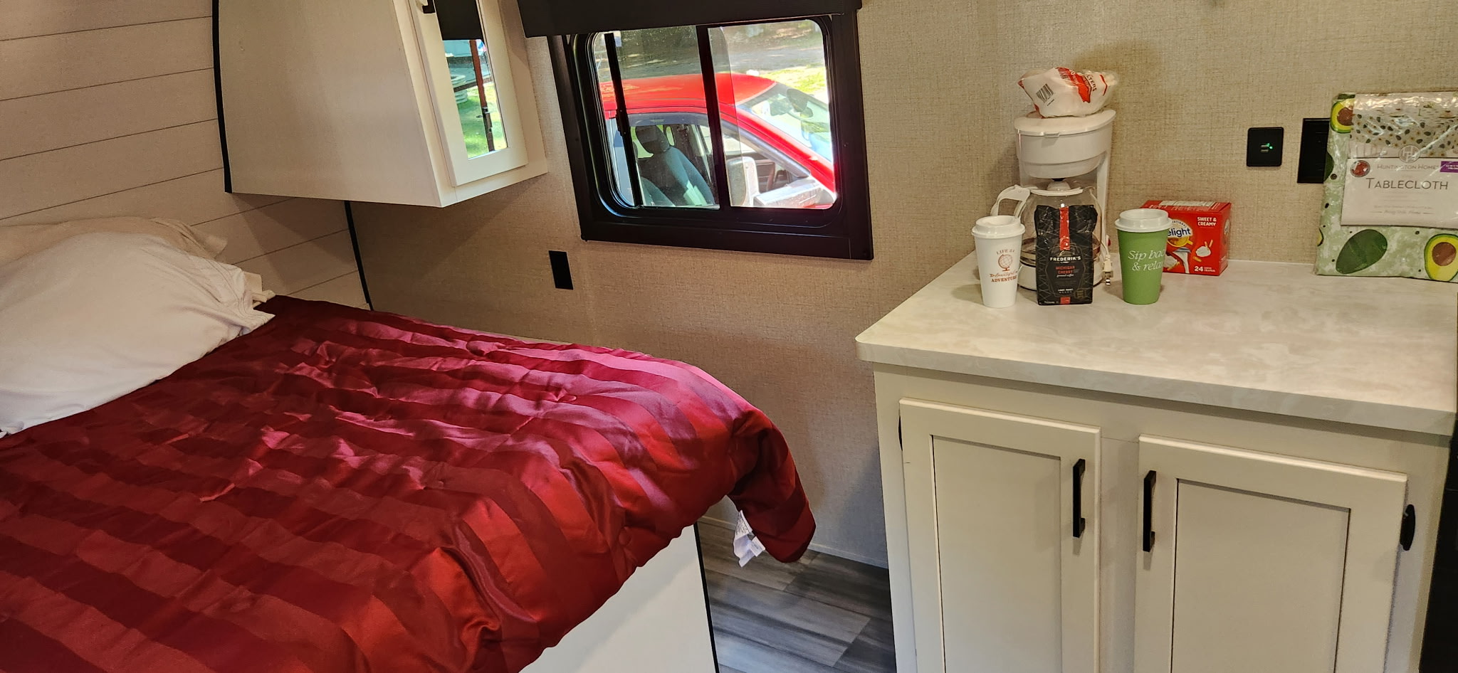 Cozy RV rental interior with a red-comforter bed and a coffee station next to the window.. Highland Ridge RV Go Play 2024