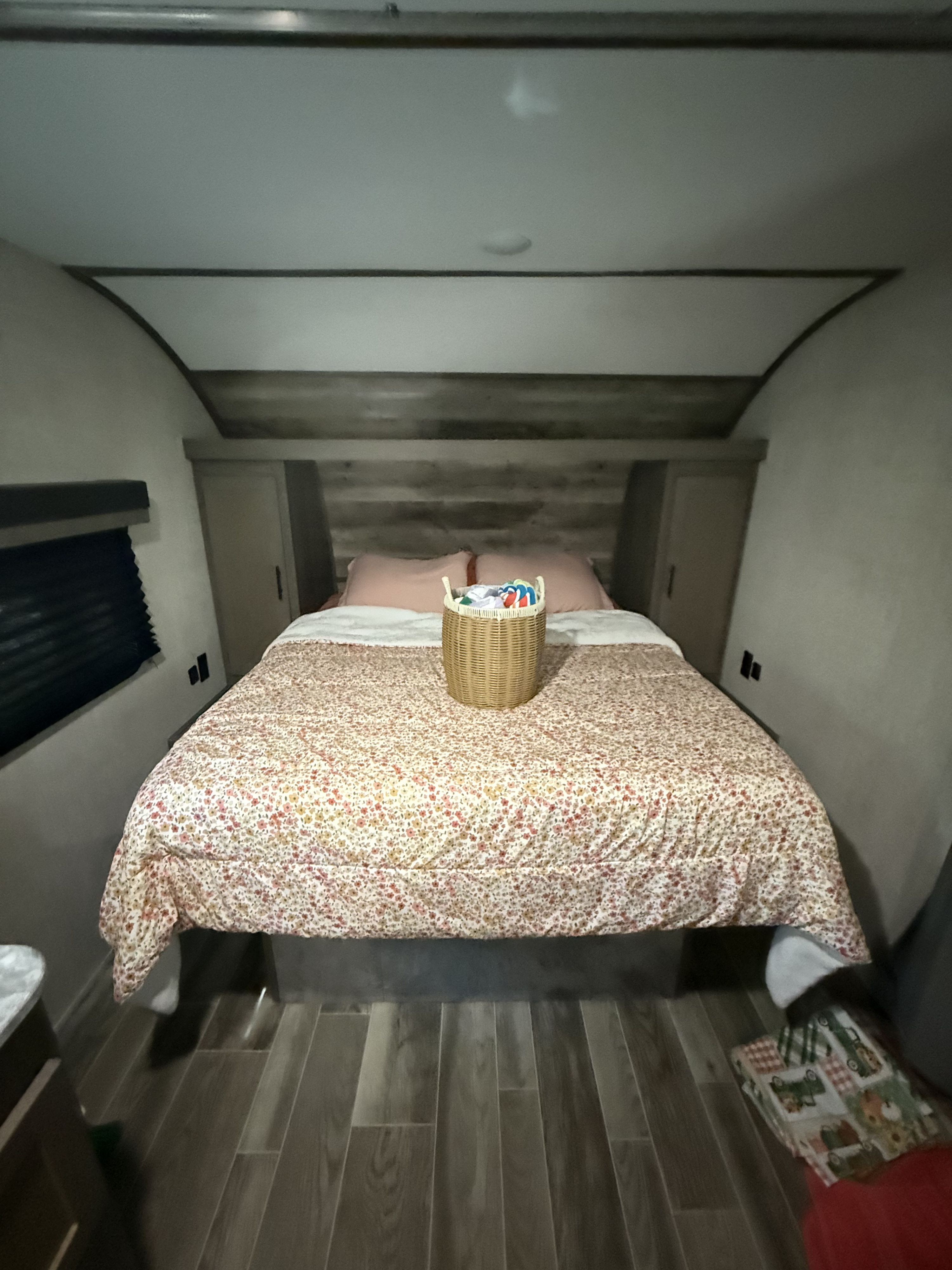 Cozy RV rental bedroom with a floral-patterned queen bed, pink pillows, built-in storage, and wood-look flooring.. Gulf Stream Ameri-Lite 2022