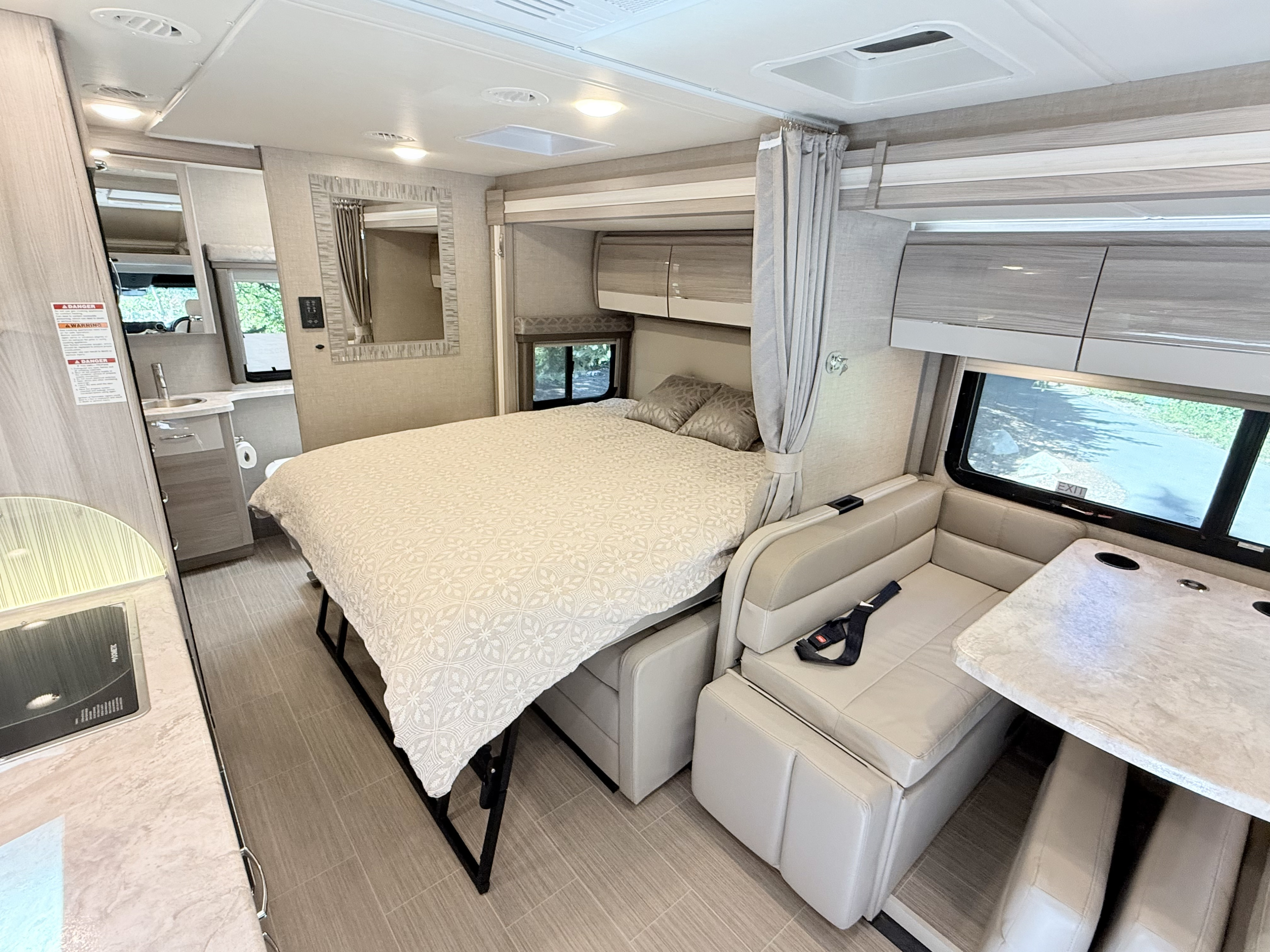 Inside an RV rental: a compact living space featuring a bed, dinette, kitchen, and partial view of the bathroom.. Thor Delano 2022