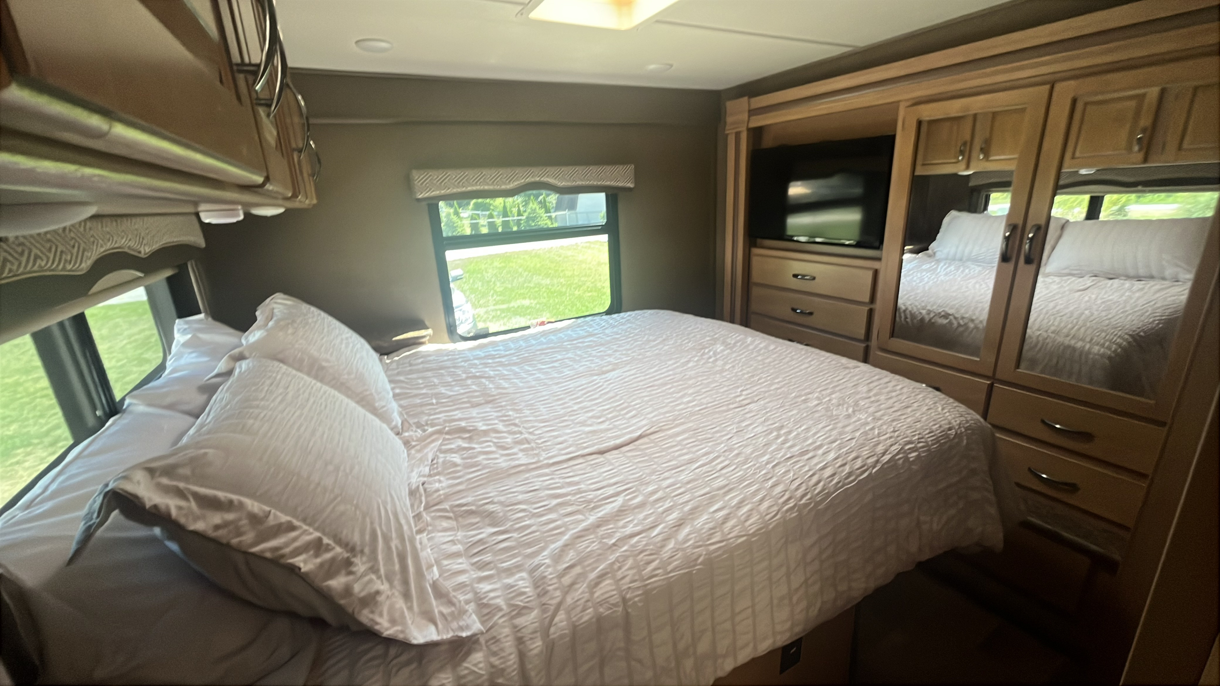 This RV rental bedroom features a cozy bed, a window with outdoor views, and built-in storage with a TV.. Thor Chateau 2017