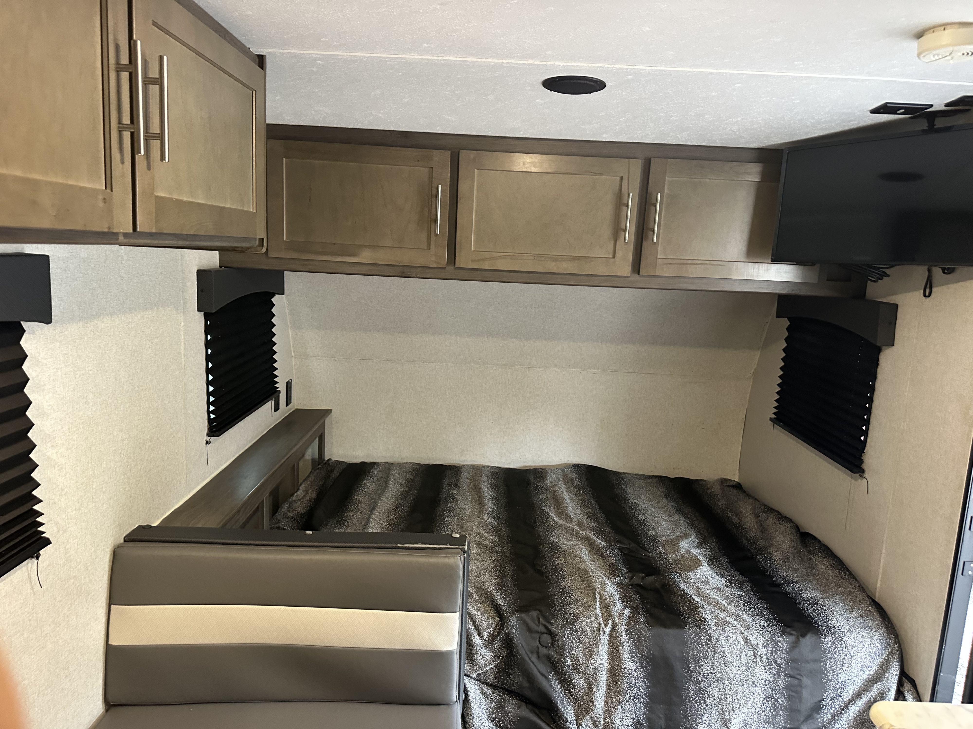 Modern RV rental interior: a cozy sleeping area with a bed, overhead cabinets, and adjacent grey seating.. Forest River Viking 2020