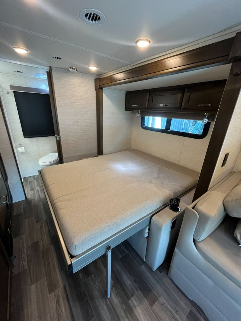 This RV rental interior features a fold-down bed with a sofa, overhead cabinets, and a bathroom entrance. Efficient compact living.. Wayfarer Wayfarer Motorhome 2021