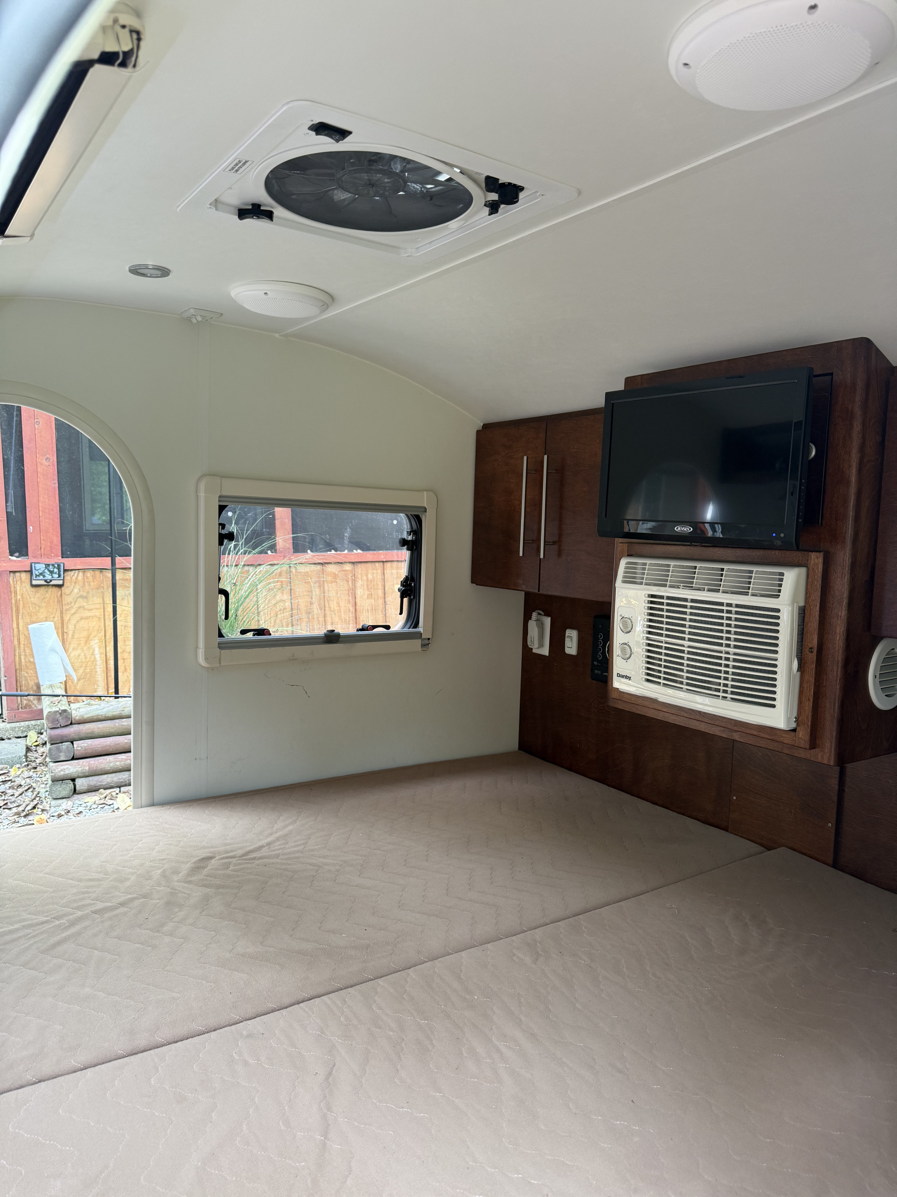 Compact rv rental interior with light-colored bed, dark wood cabinets, mounted TV, and window AC unit.. nuCamp T@G 2020