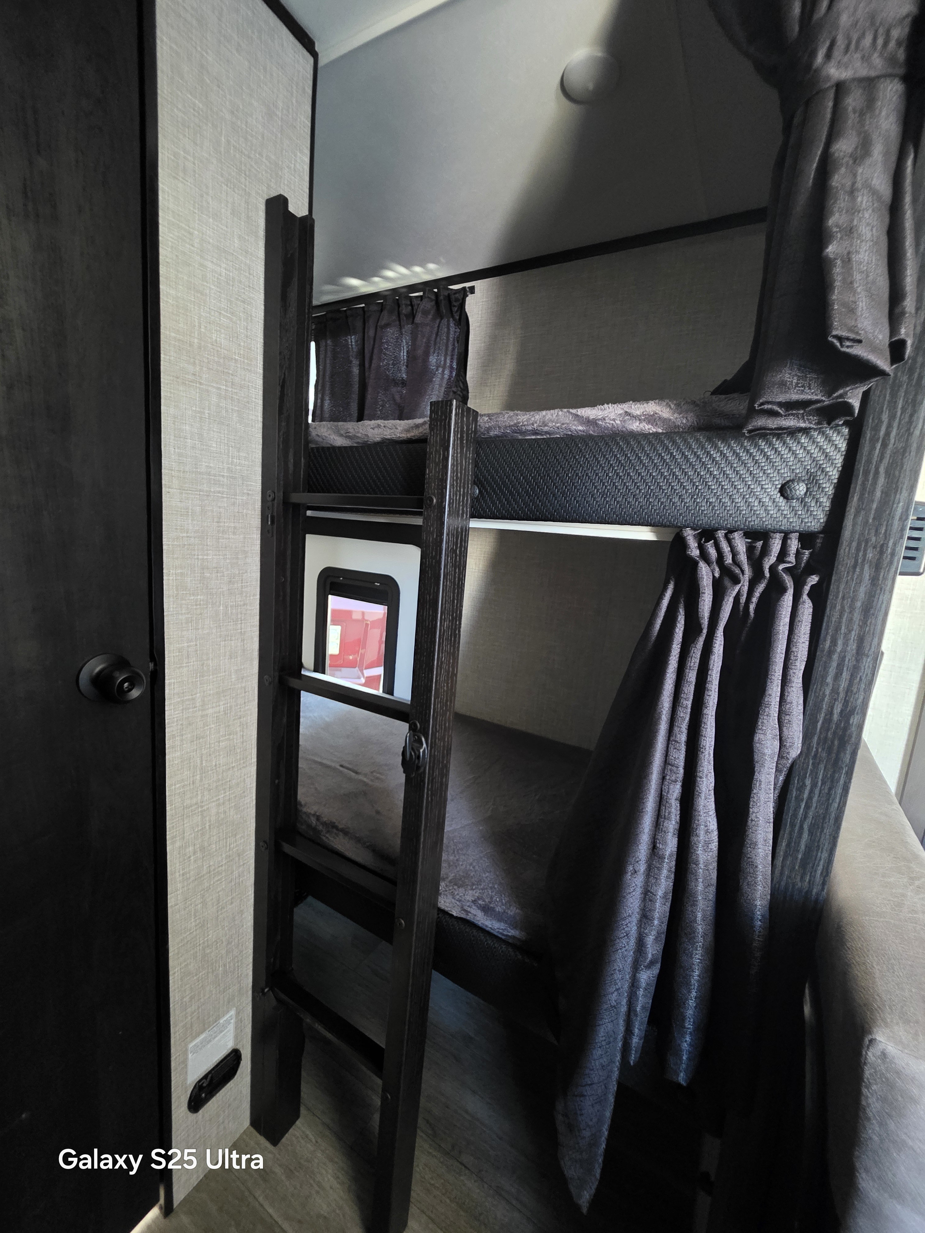 Cozy dark wood bunk beds with privacy curtains and a ladder inside an RV rental, offering compact sleeping space.. Jayco Jay Feather Micro 2023