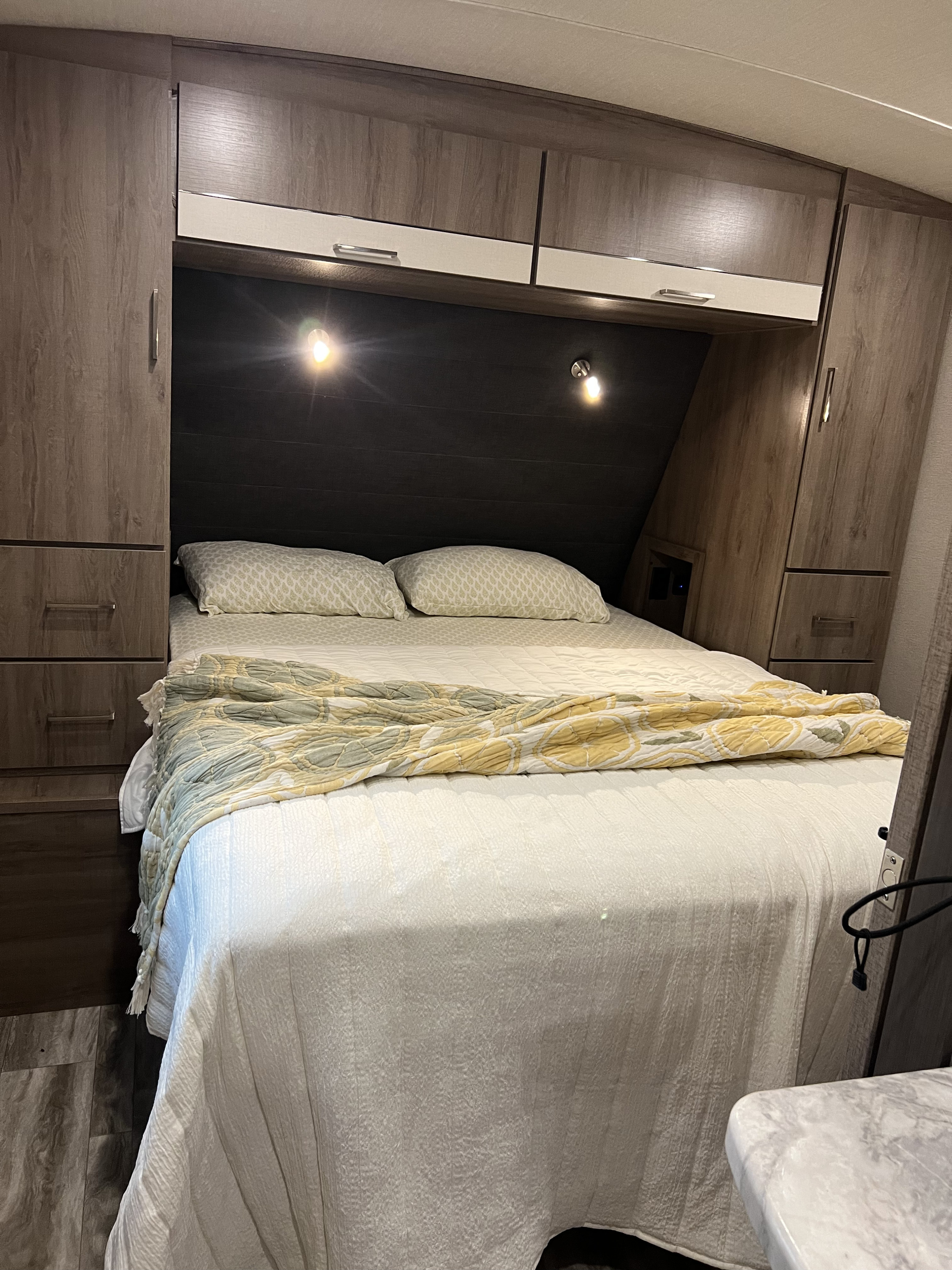 Cozy RV rental bedroom featuring a comfortable bed with a patterned throw blanket, built-in storage, and reading lights.. Grand Design Imagine 2023