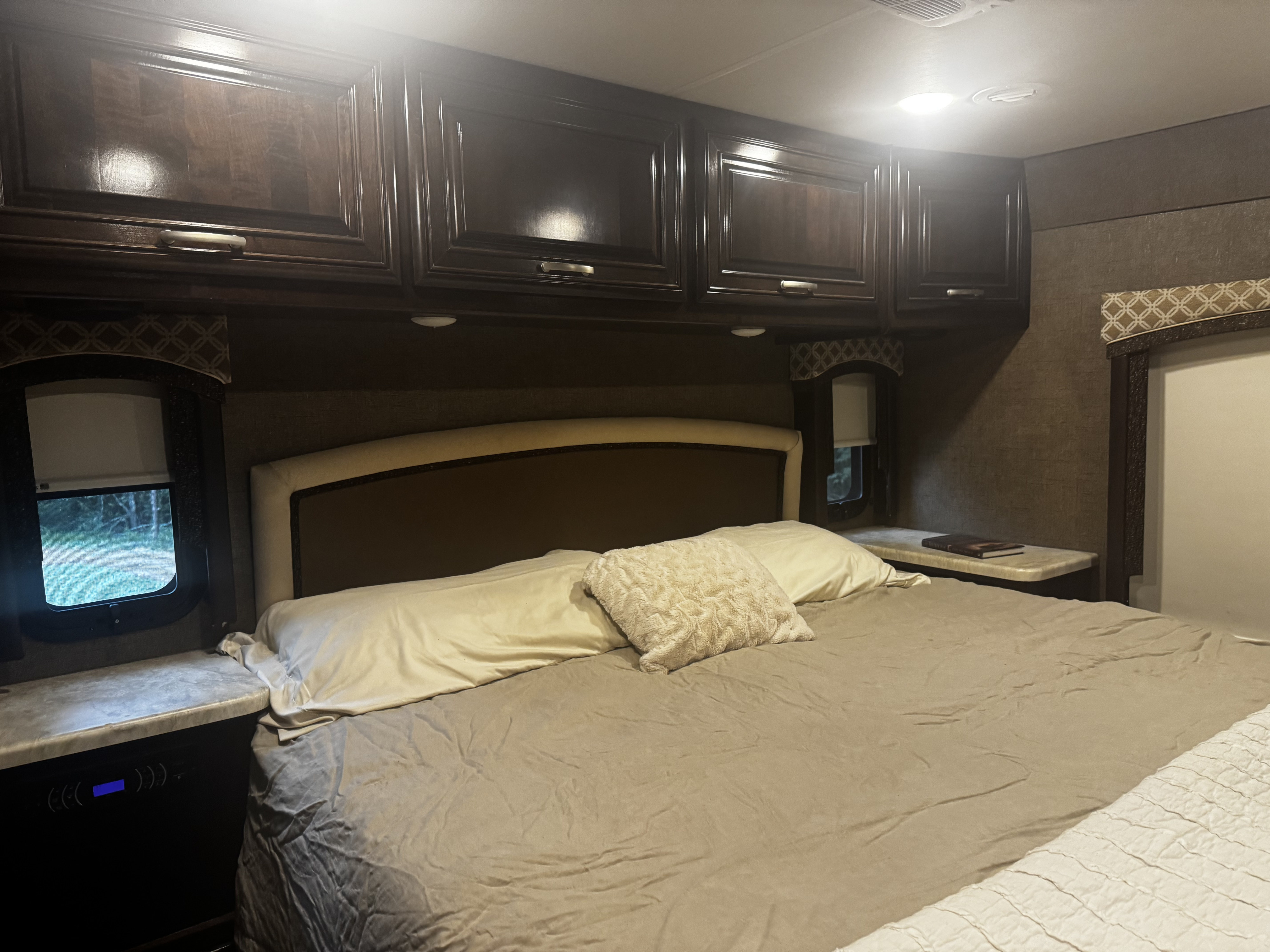 Cozy RV rental bedroom featuring a comfortable bed, dark wood overhead storage, and windows with nightstands.. Thor Chateau 2017