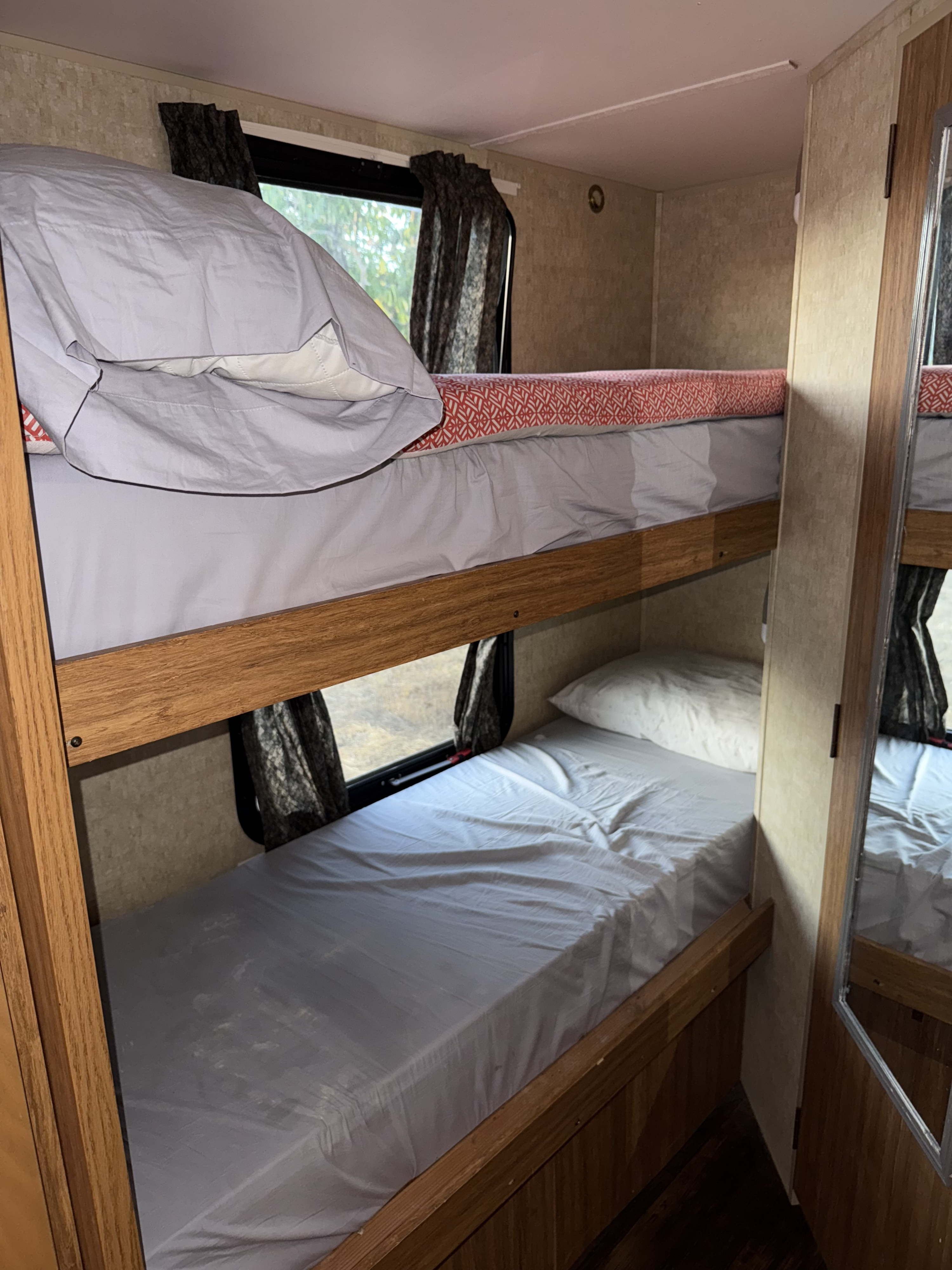 Inside an RV rental: two bunk beds with simple bedding, curtains, and a mirror on the side, providing sleeping space.. Skyline Eco Camp 2013