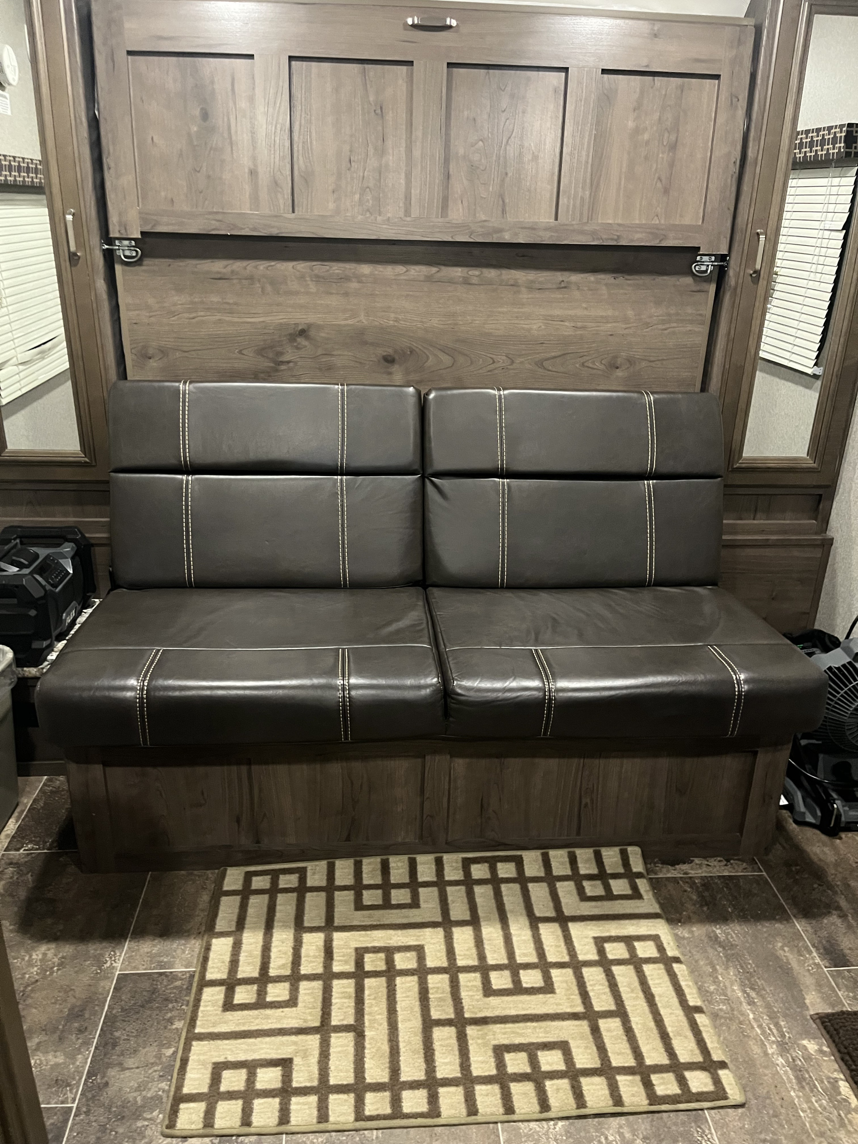 RV rental: Dark leather-look sofa/dinette with white stitching, wood paneling (concealed murphy bed), and geometric rug.. Keystone RV Passport 2019