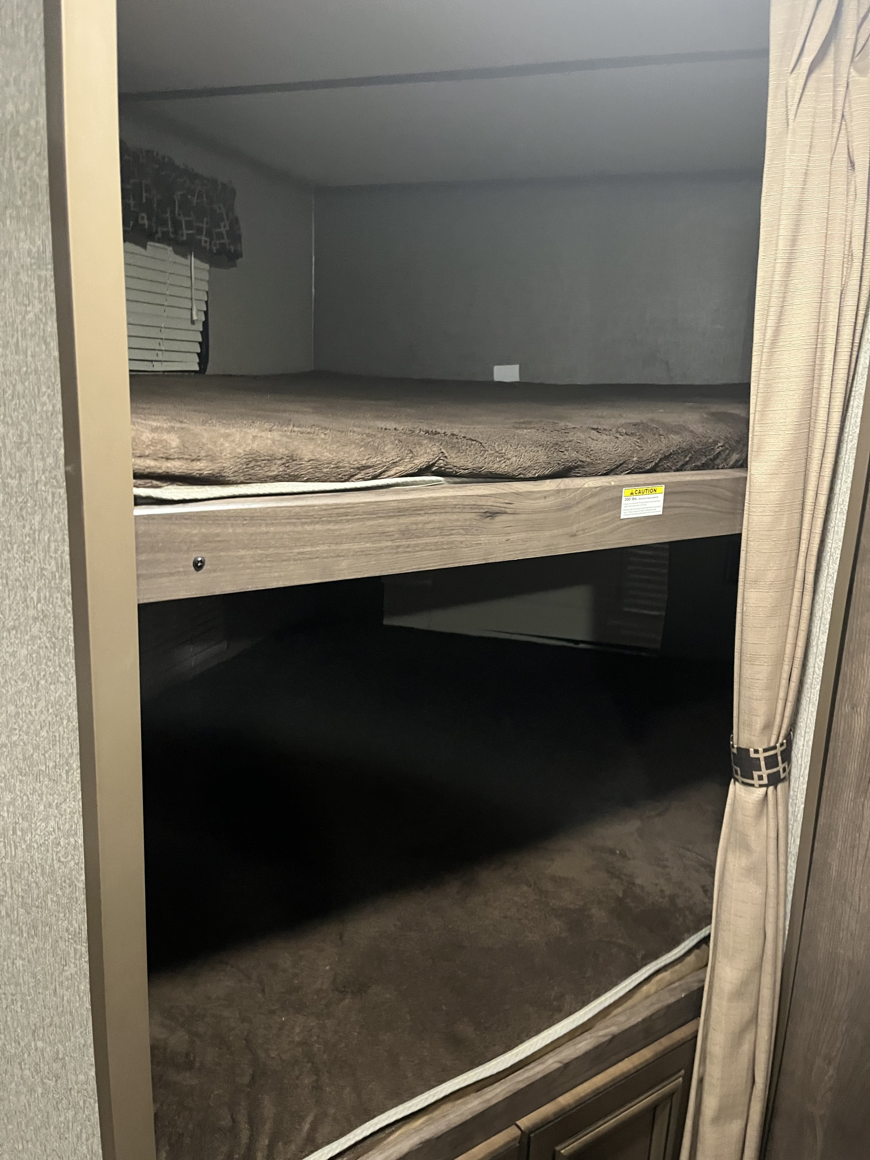 RV rental bunk beds: two compact sleeping berths with brown bedding, a sturdy wooden frame, and a visible caution label.. Keystone RV Passport 2019