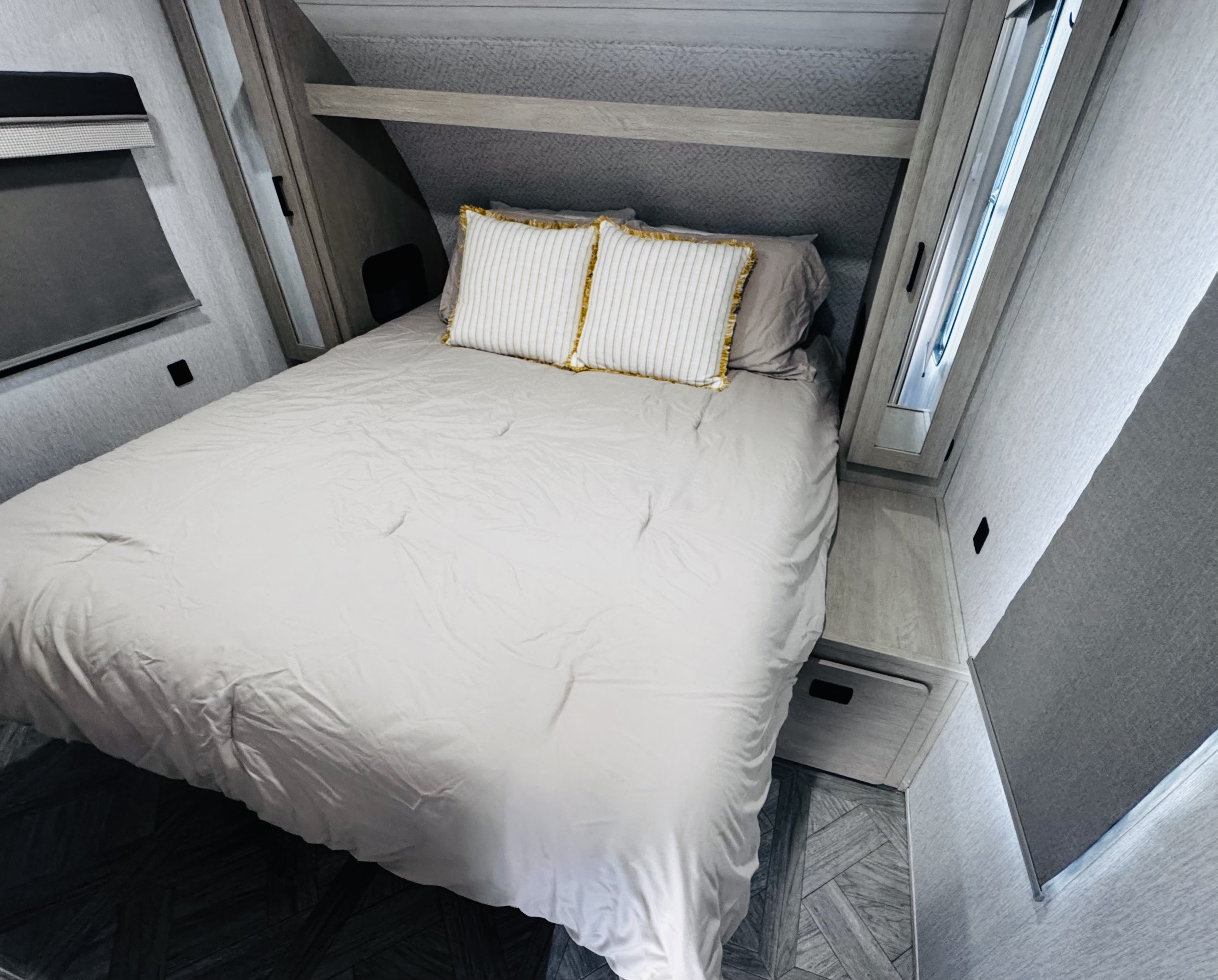 Comfortable bed setup in a modern RV rental, featuring light grey bedding, decorative pillows, and built-in storage for travel.. Forest River Wildwood X-Lite 2023