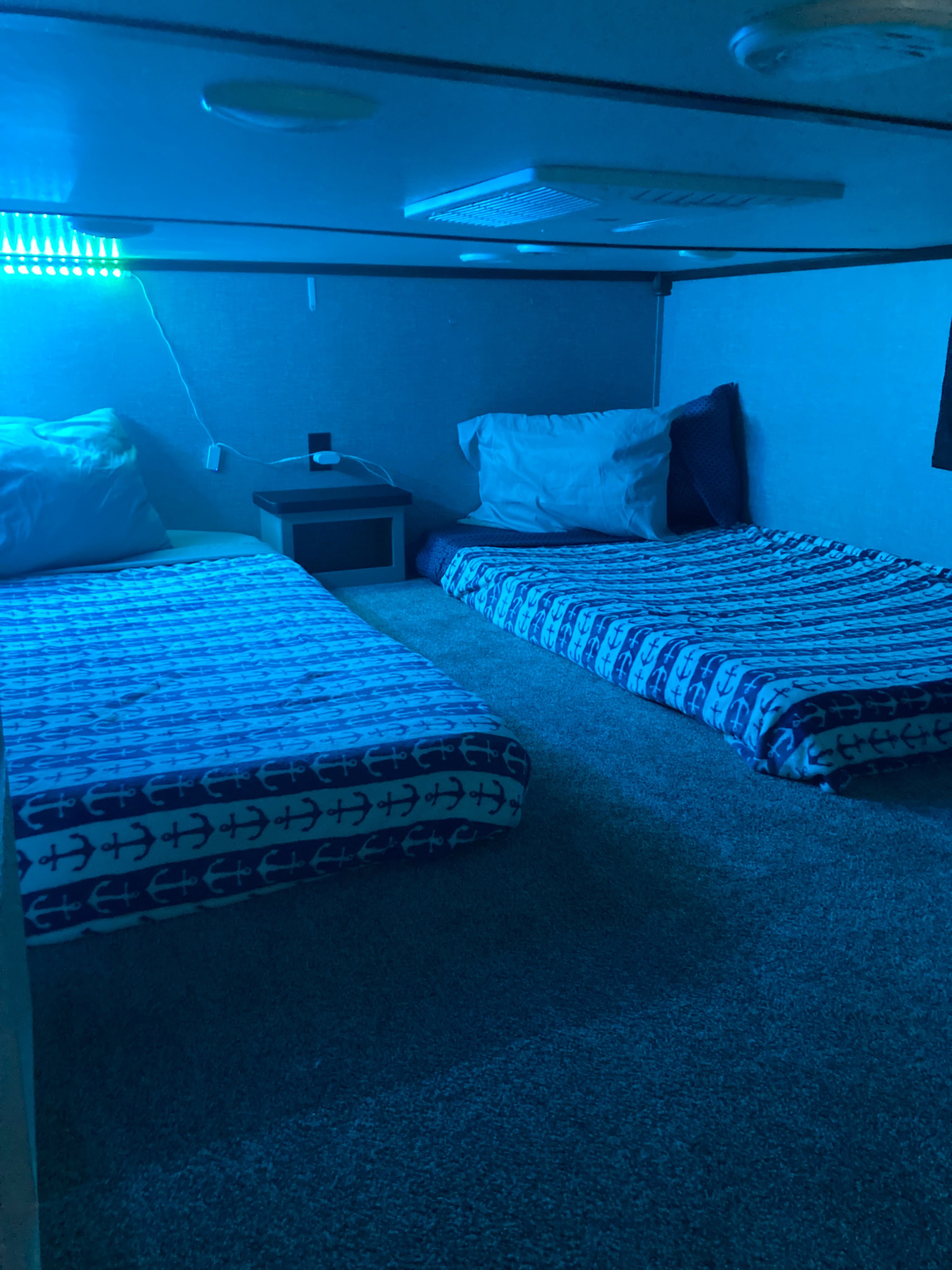 RV rental: Cozy bunk sleeping area with two beds on floor, blue LED lighting, anchor-themed blankets, and a nightstand.. Crossroads RV Hampton 2020
