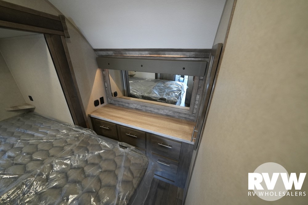 Explore this clean & modern RV rental bedroom featuring a bed with protective cover, built-in mirror, and drawers for storage.. Forest River XLR Boost Toy Hauler 2020