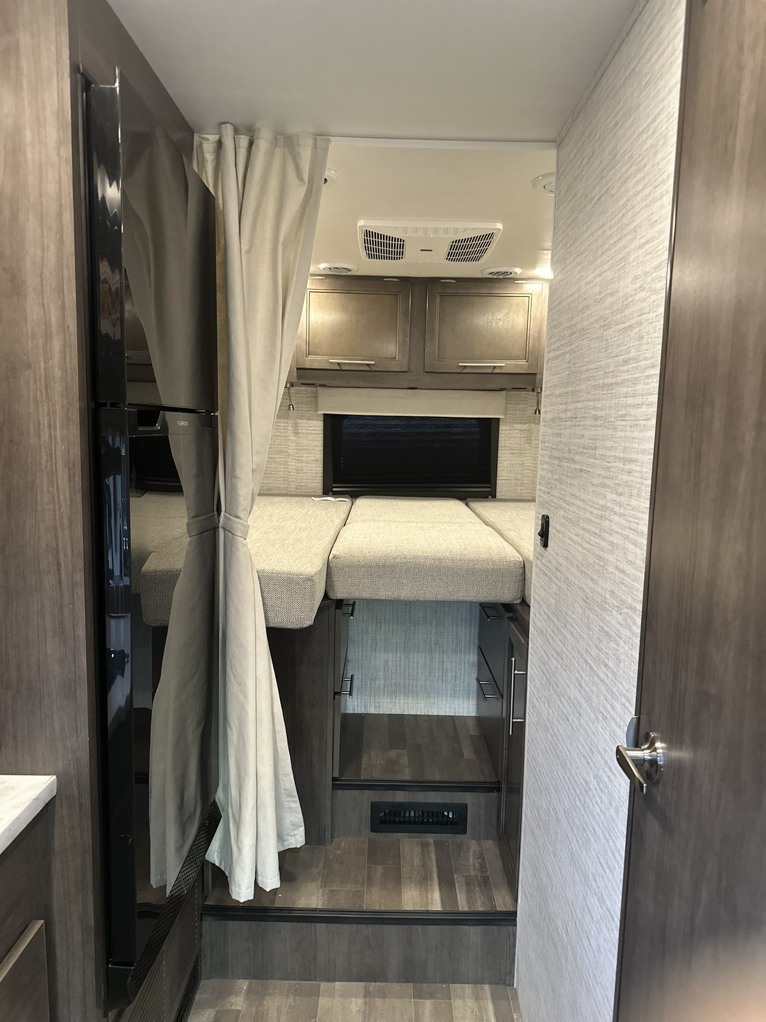Interior view of an RV rental showing compact bunk beds, a drawn privacy curtain, refrigerator, and overhead cabinets in a modern design.. JAYCO REDHAWK SE 22TF 2025