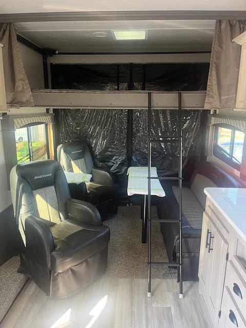 Spacious RV rental interior featuring a bunk bed with ladder, reclining chairs, and a dining area.. Forest River Shockwave 2023