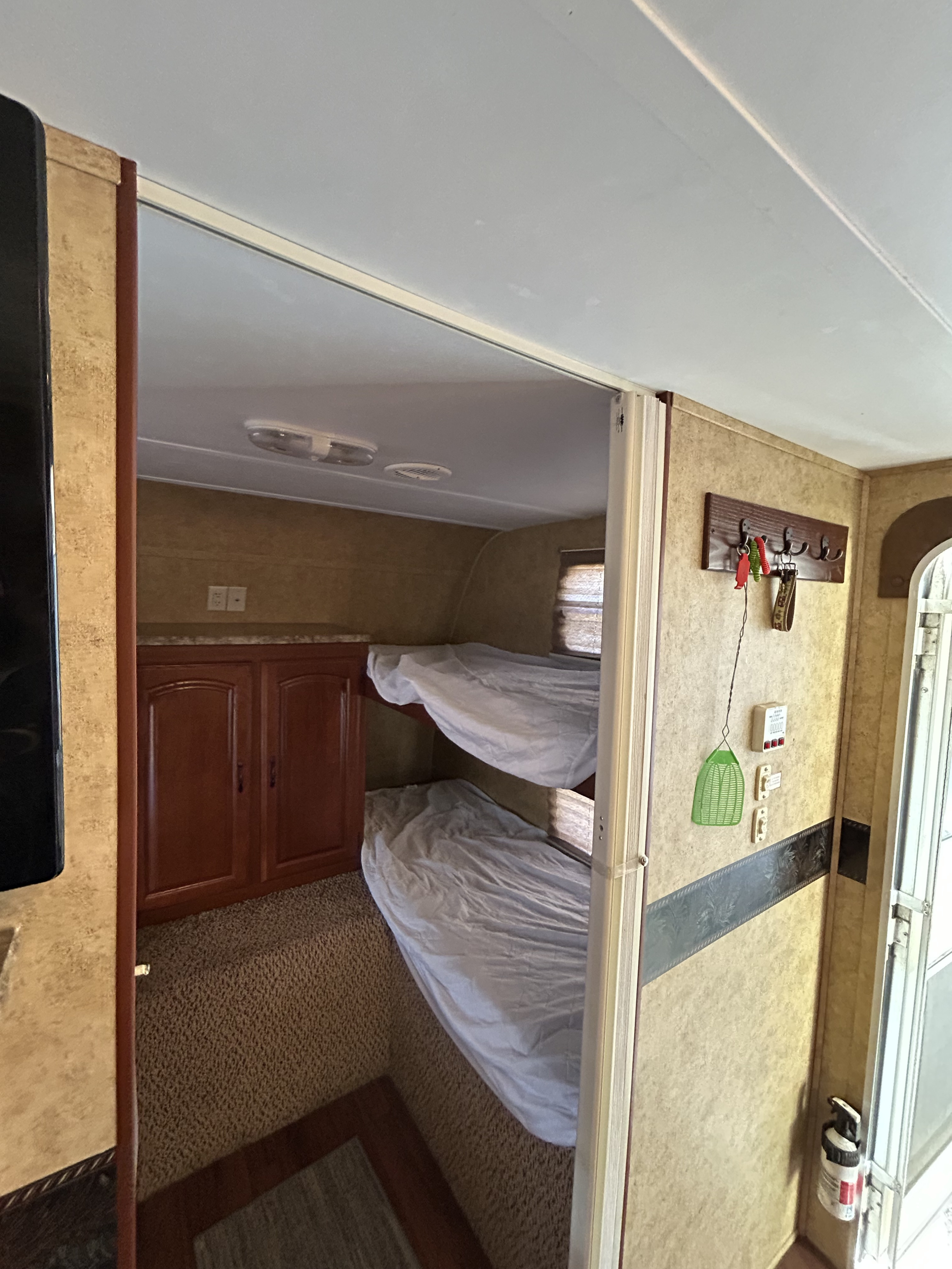 An RV rental's sleeping area features bunk beds, lower cabinetry, and essentials like a key rack and fire extinguisher.. Keystone RV Outback 10th Anniversary 2011