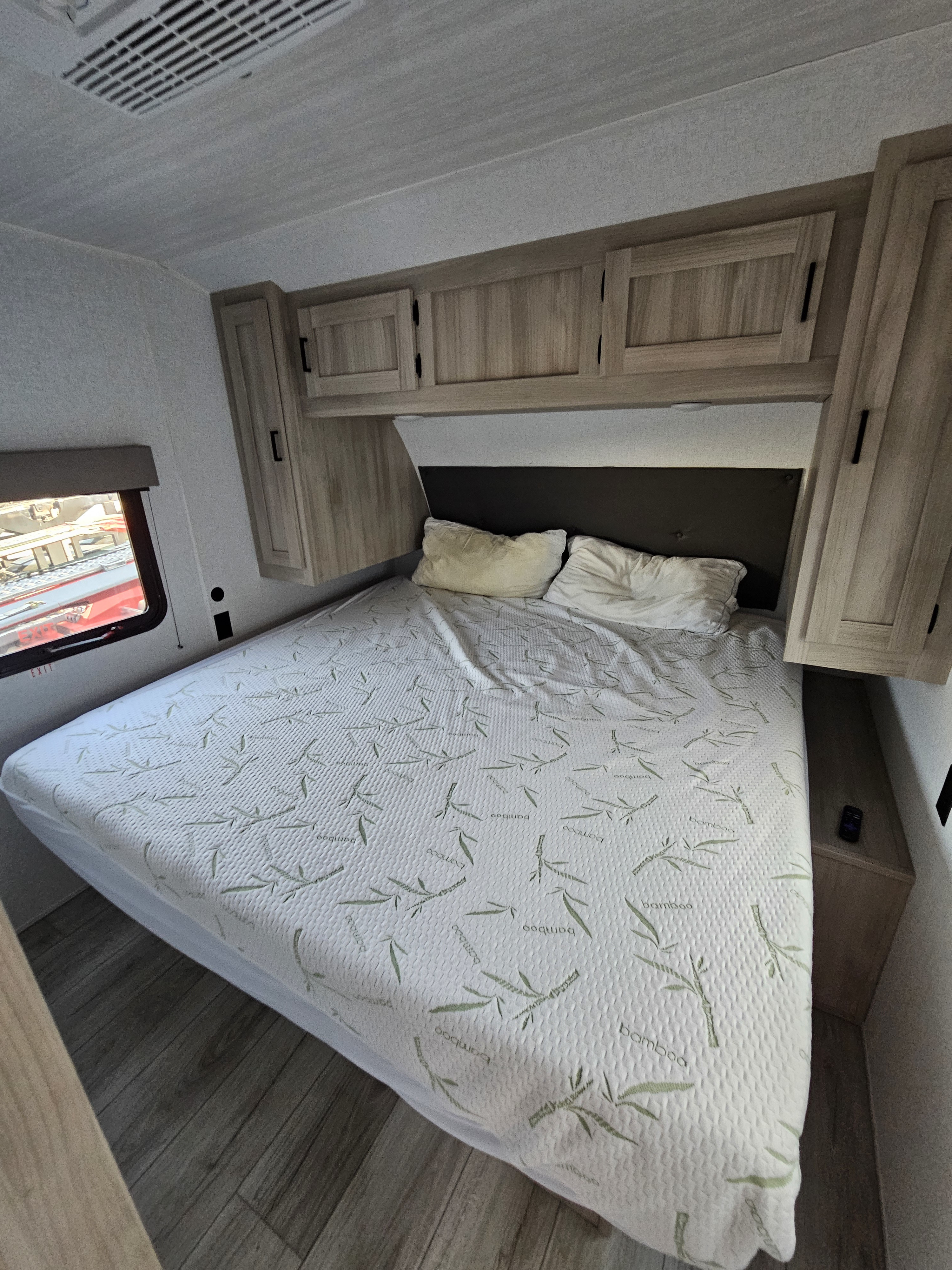 RV rental bedroom featuring a comfortable bed with a bamboo mattress cover, overhead storage, and a window for scenic views.. East to West 271bh 2024