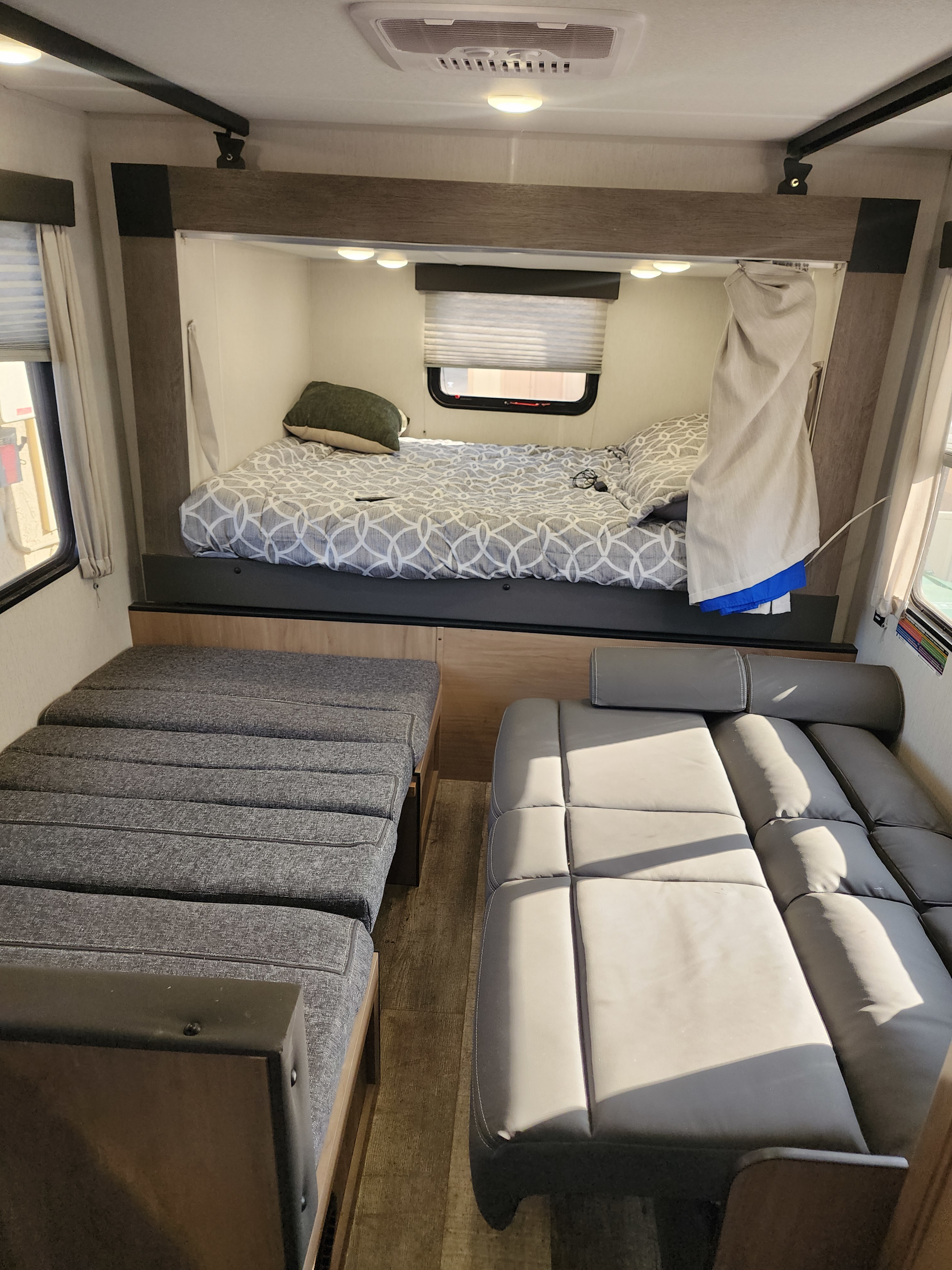 RV rental interior: A cozy bedroom area with a patterned comforter, alongside a gray fabric dinette and a plush sofa.. Forest River GREY WOLF 2024