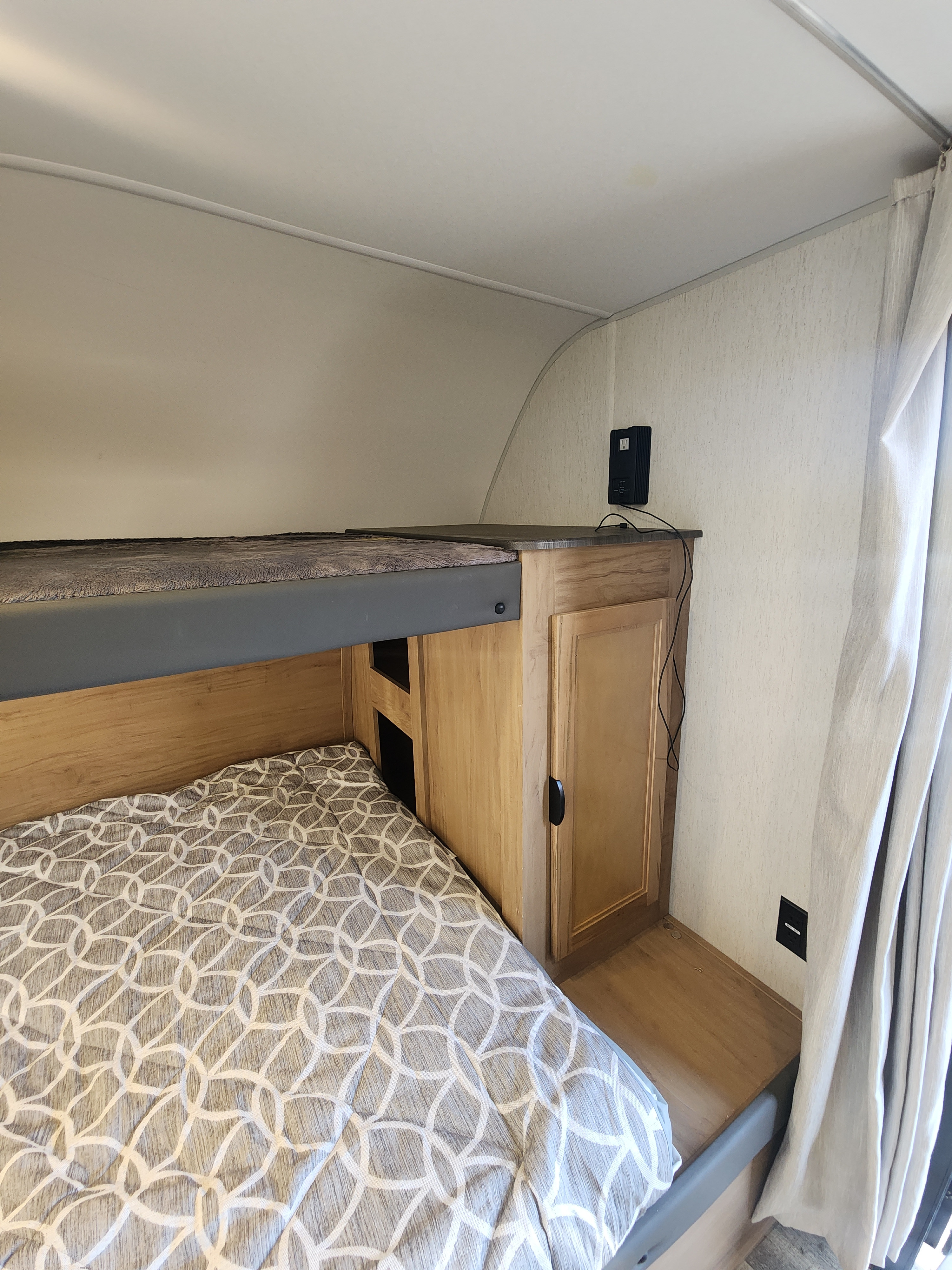 Comfortable bunk beds with patterned bedding, built-in storage, and a power outlet, perfect for an RV rental.. Forest River GREY WOLF 2024