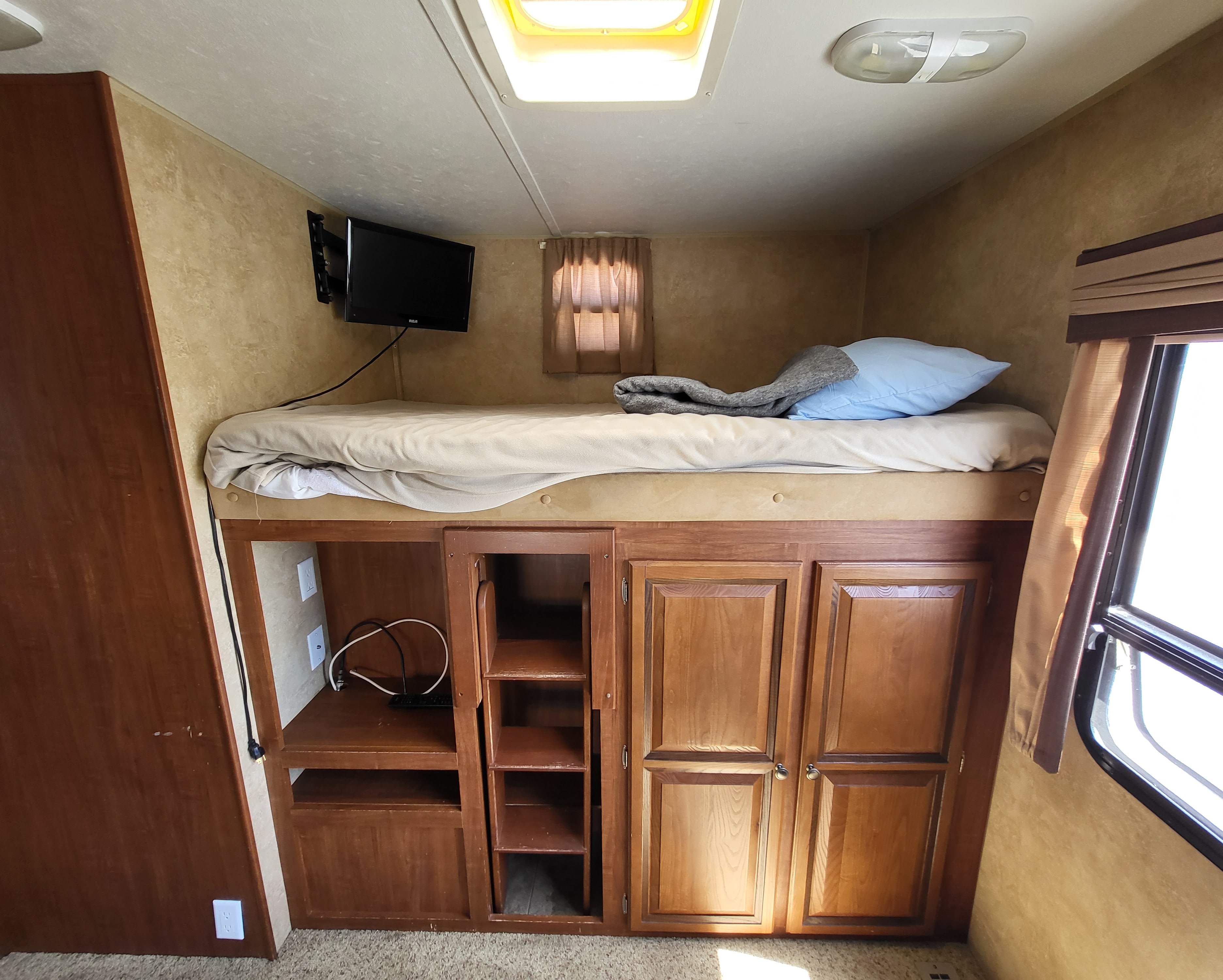 Cozy RV rental interior featuring a bunk bed with a TV, a skylight, and built-in storage cabinets below.. Jayco Eagle Super Lite 2012