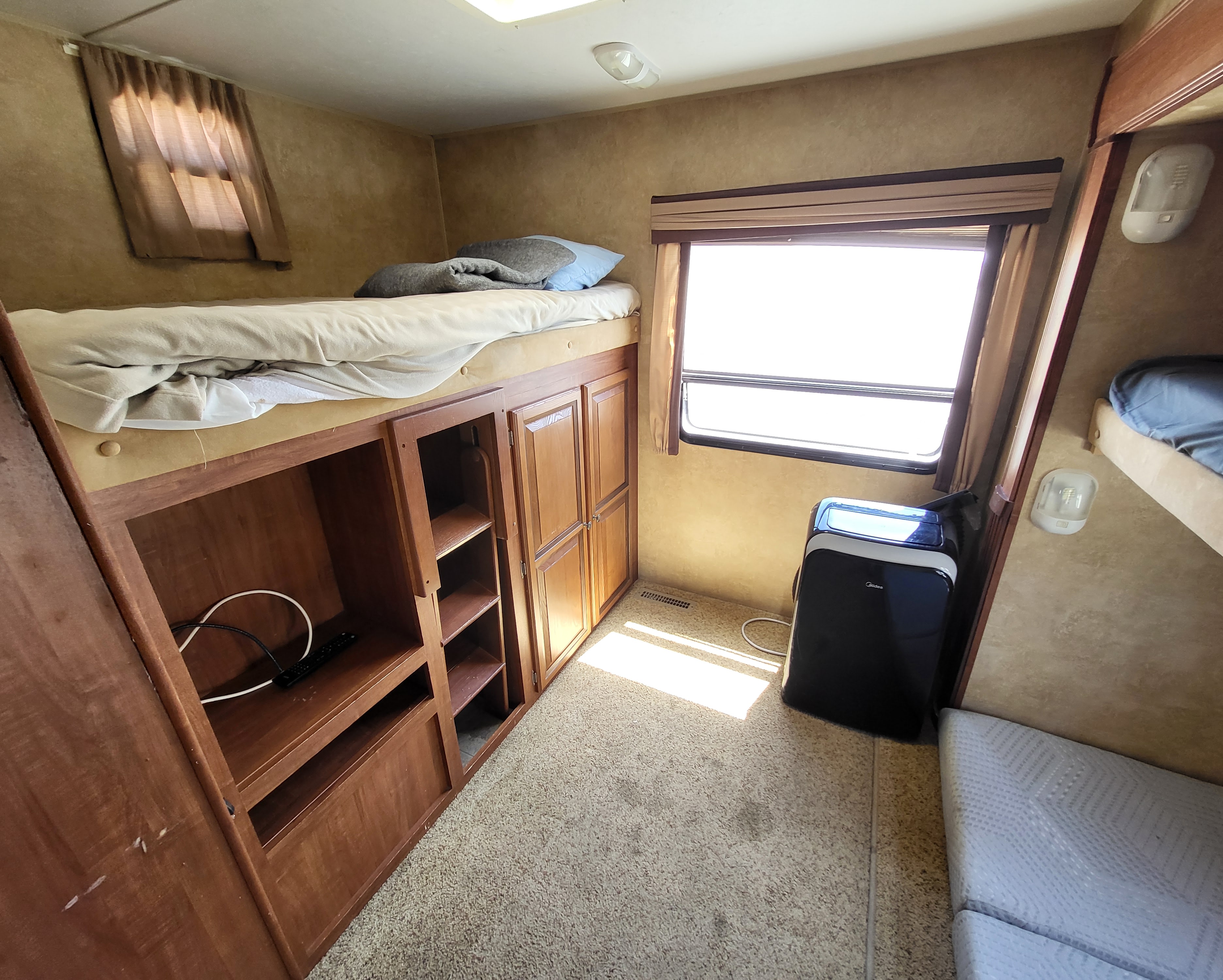 Cozy RV rental interior featuring an upper bunk bed, wooden storage units, and a portable AC unit for comfort.. Jayco Eagle Super Lite 2012