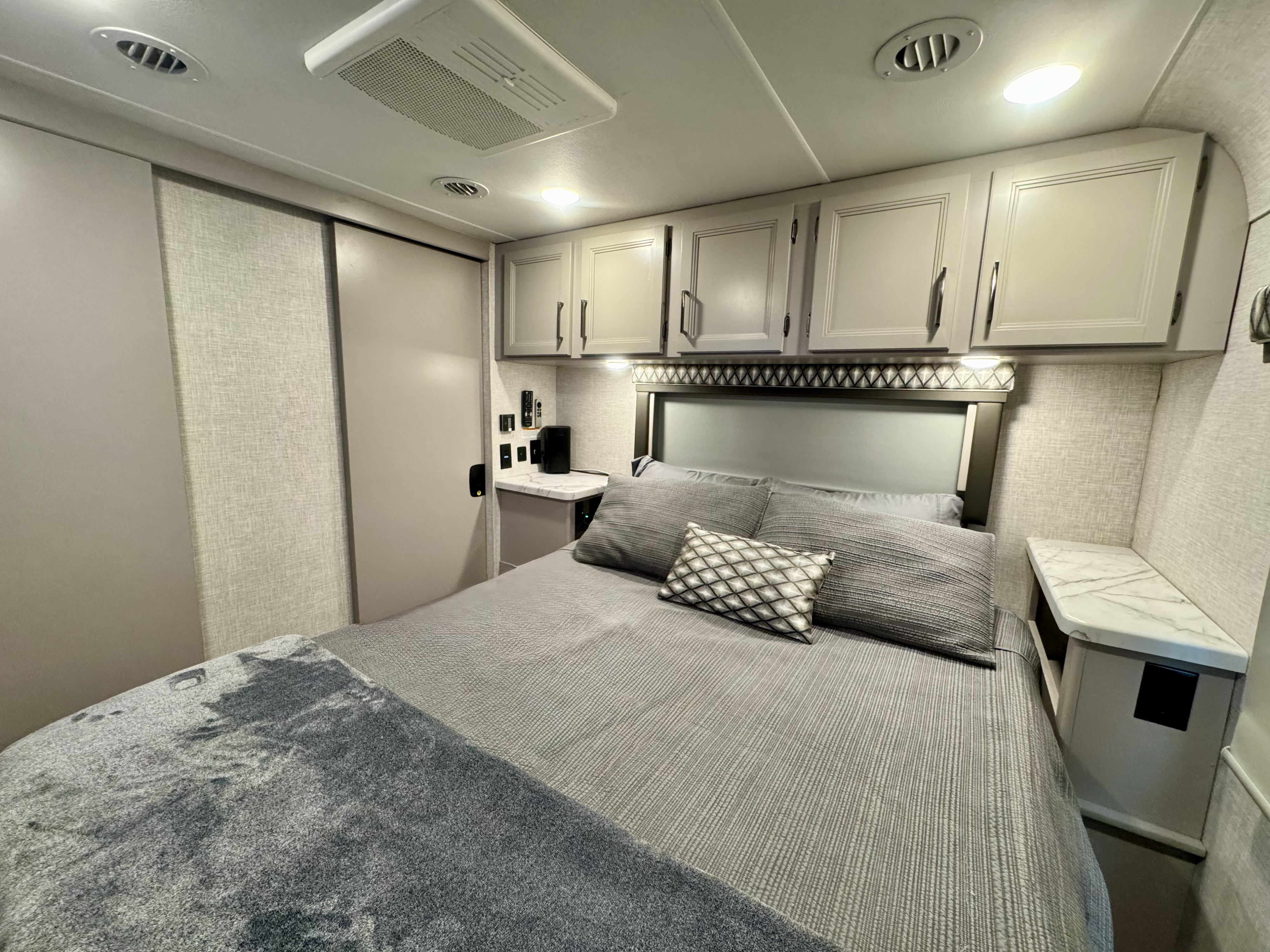 Cozy RV rental bedroom featuring a comfortable bed, overhead storage, and modern gray decor.. Thor Geneva 2023