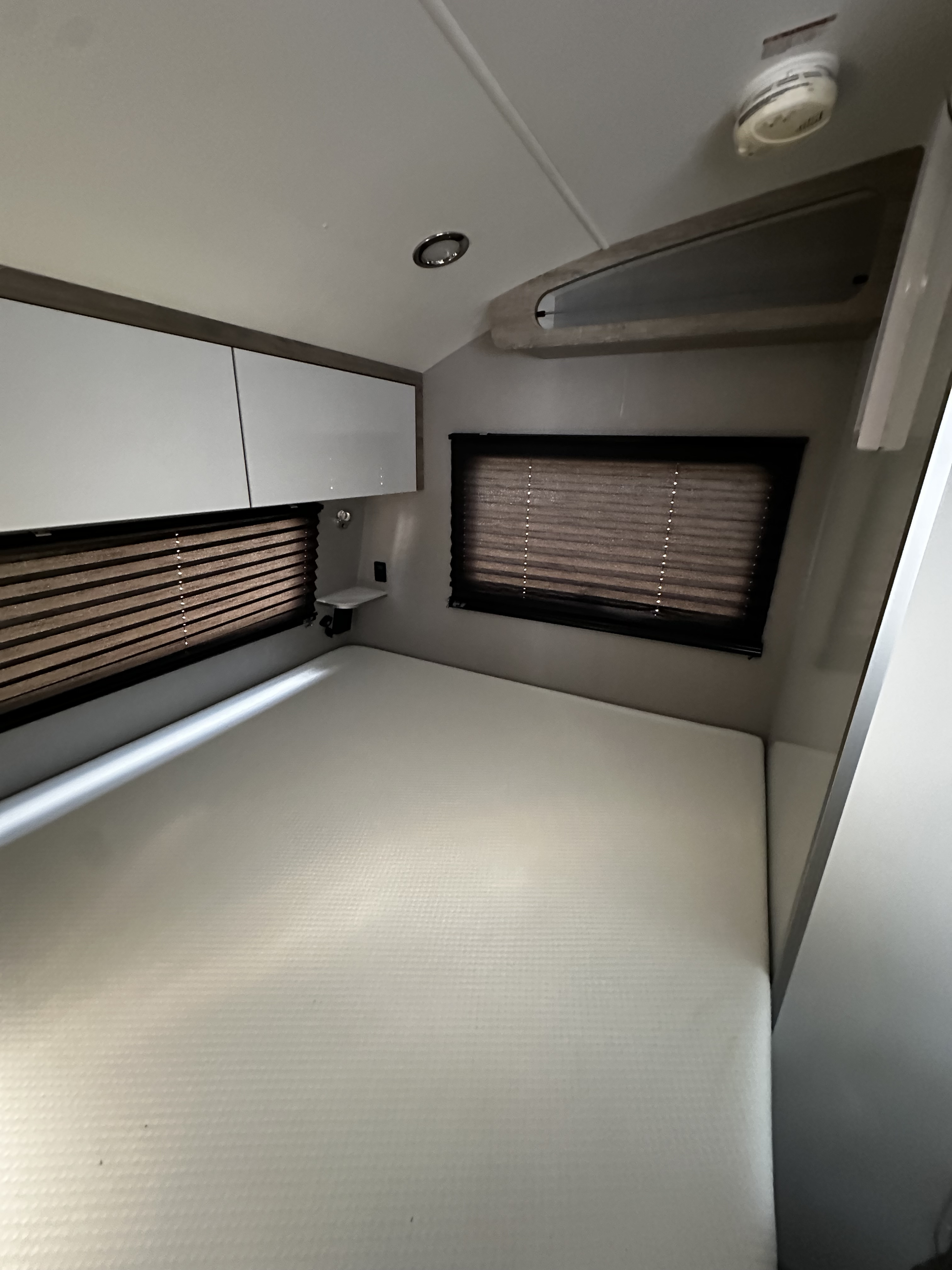 Modern RV rental sleeping area with a white mattress, sleek overhead cabinets, and dark window blinds.. InTech RV Sol 2023