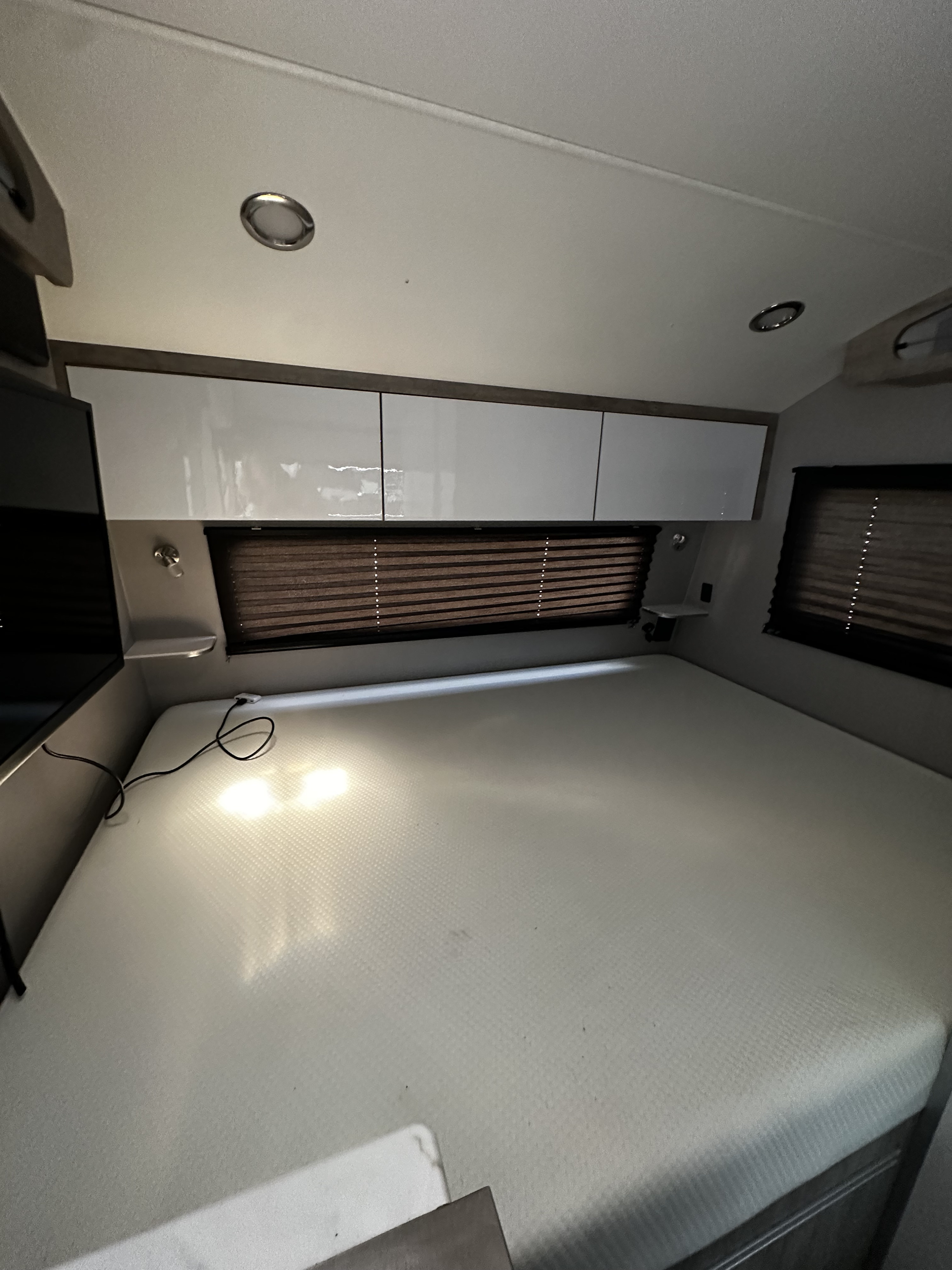 RV rental bedroom featuring a spacious mattress, bright overhead cabinets, and practical window blinds.. InTech RV Sol 2023