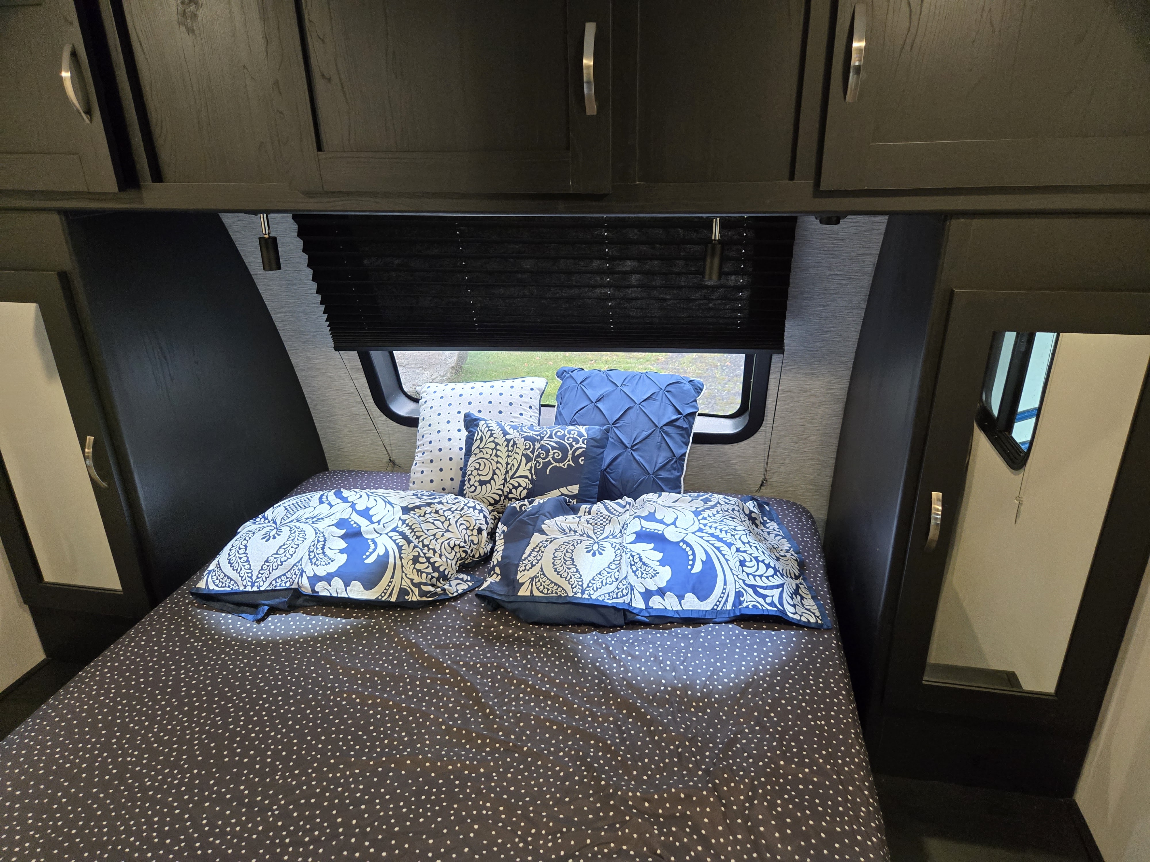Cozy RV rental bedroom featuring a bed with blue and white patterned bedding, overhead cabinets, and mirrored storage.. Forest River Coachmen Freedom Express Ultra Lite 2022