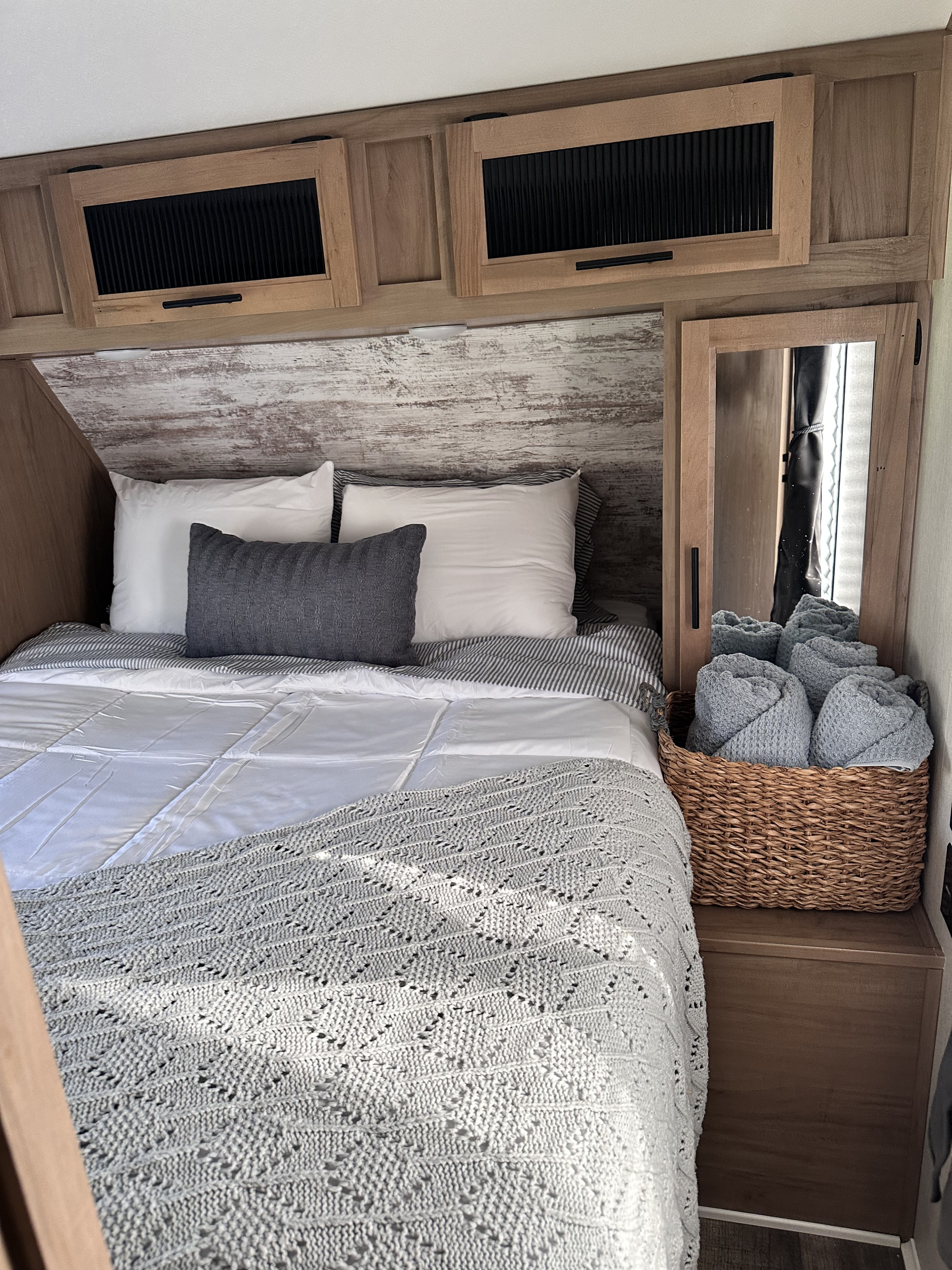 Comfortable RV rental interior featuring a neatly made bed, overhead cabinets, and soft towels in a woven basket.. Forest River Cherokee Alpha Wolf 2023