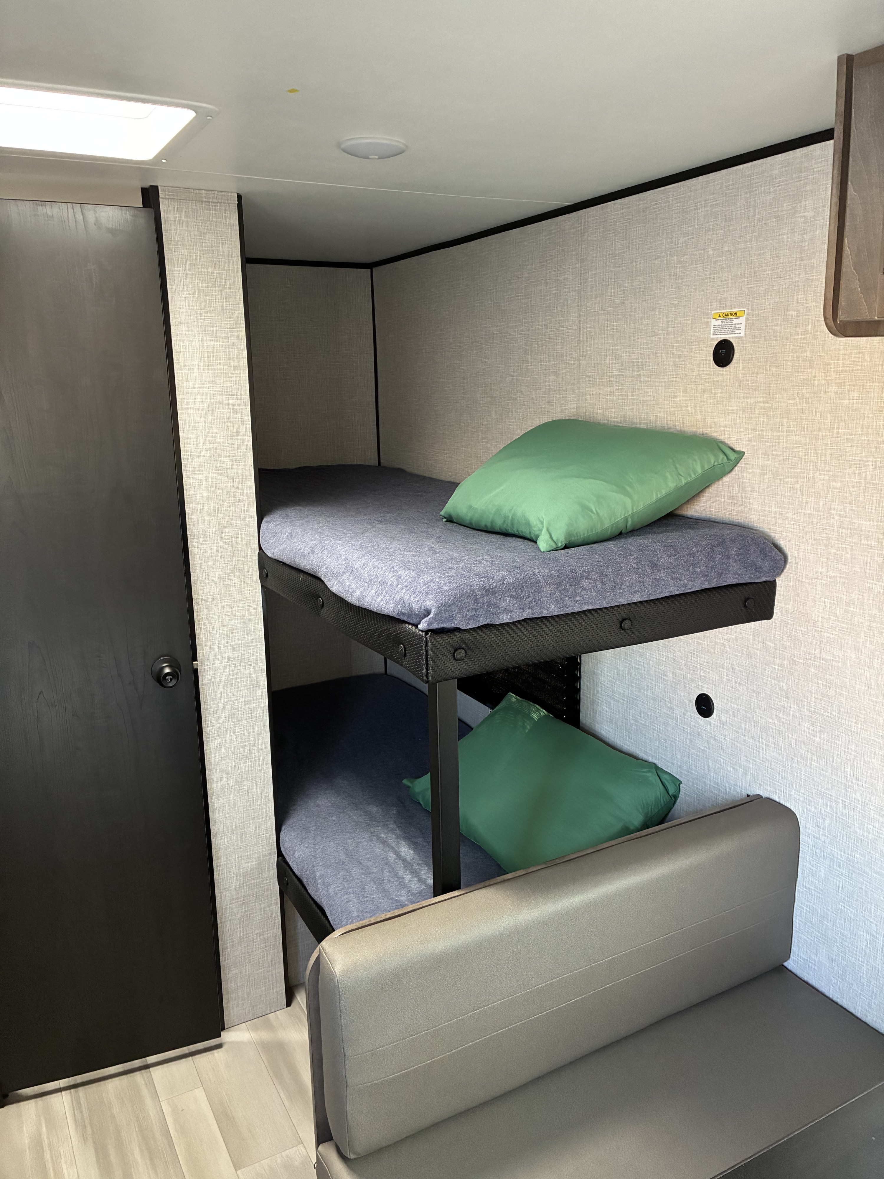 Interior of an RV rental with comfortable bunk beds featuring blue sheets and green pillows, alongside a cozy grey bench.. Starcraft Ar-One 2026