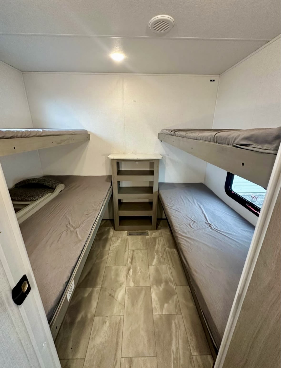 This RV rental bunk room has two sets of bunk beds with gray bedding, a central shelf unit, and a light-tiled floor.. Dutchmen Kodiak 2025