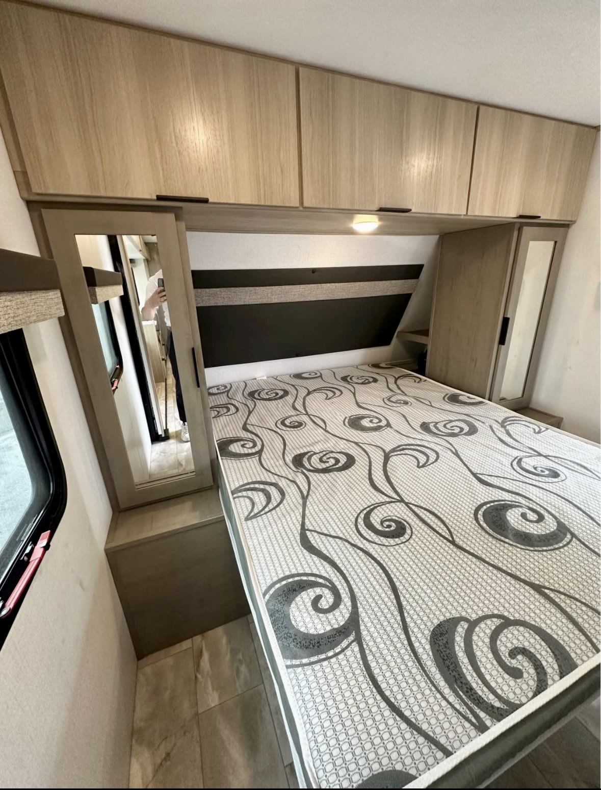 This RV rental bedroom offers a comfortable bed, ample overhead storage, and a handy mirror.. Dutchmen Kodiak 2025
