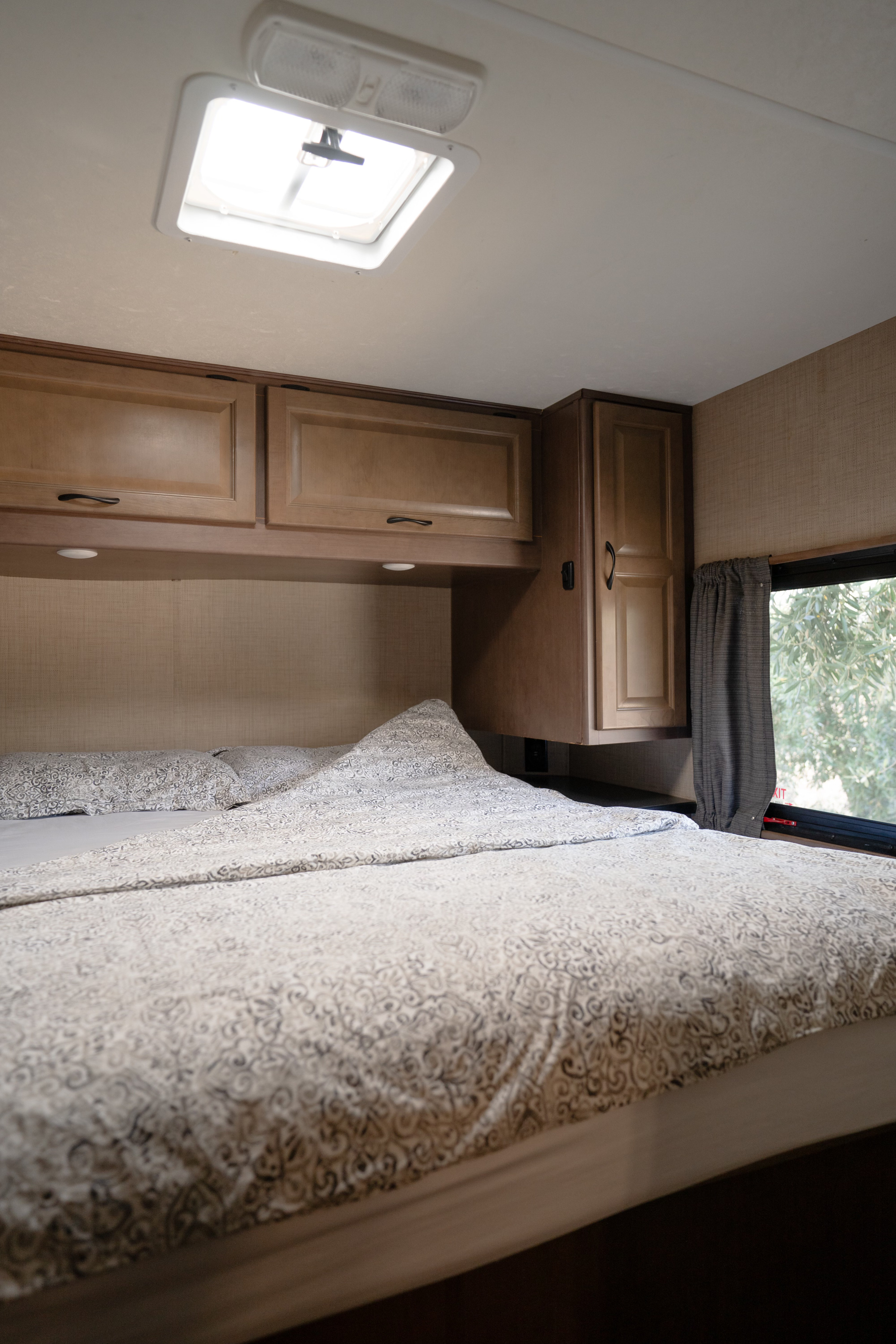 Cozy RV rental bedroom with patterned bedding, overhead cabinets, and a bright ceiling vent and window view.. Winnebago Minnie Winnie 2020