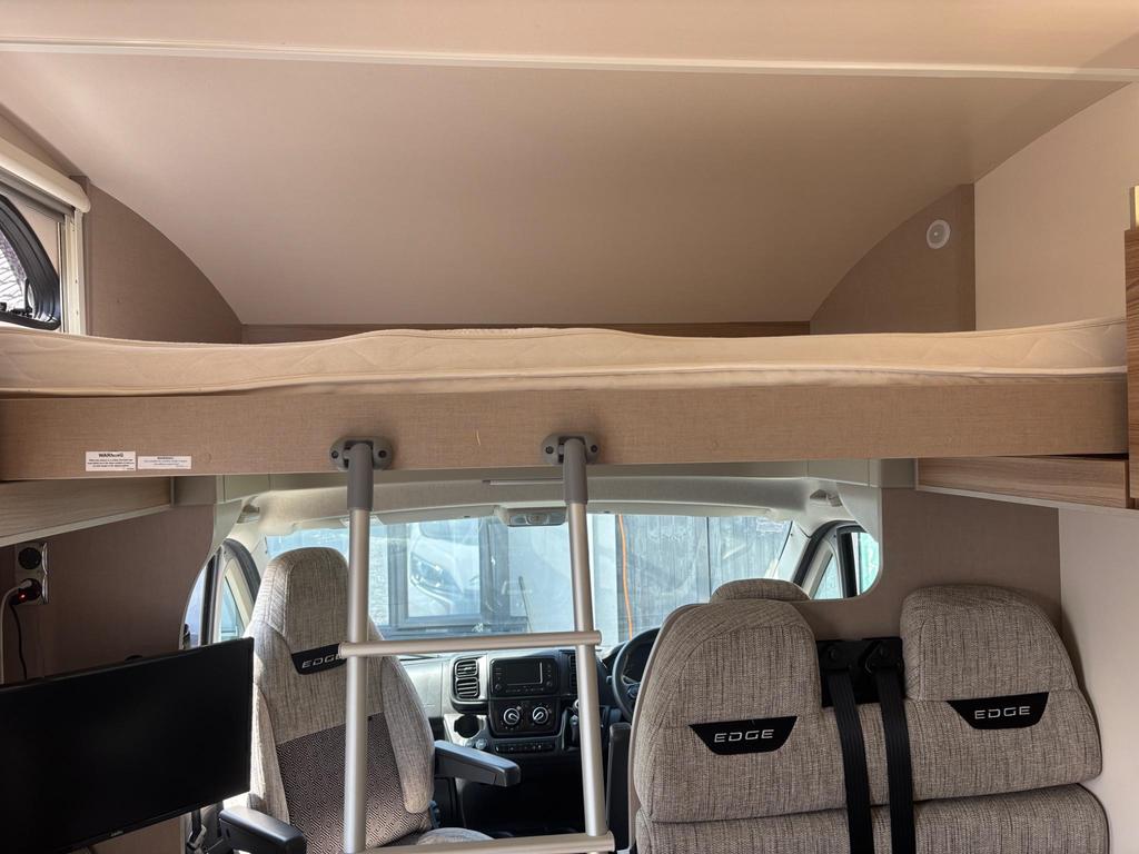 RV rental interior: front view with overhead bunk bed, ladder, and driver's cabin seats featuring 'EDGE' branding.. Swift Edge 466 2020