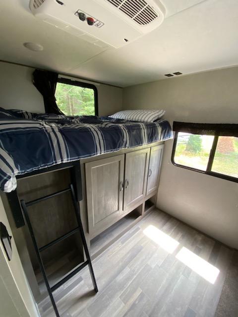 This rv rental features a cozy bunk bed, convenient ladder, and ample storage, plus AC and window views.. Forest River Vibe 2020