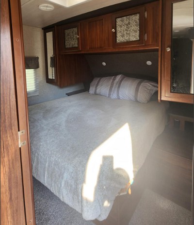 This RV rental bedroom features a comfortable bed, overhead cabinets, and a window, ideal for restful sleep on your travels.. Heartland RVs Mallard 2018
