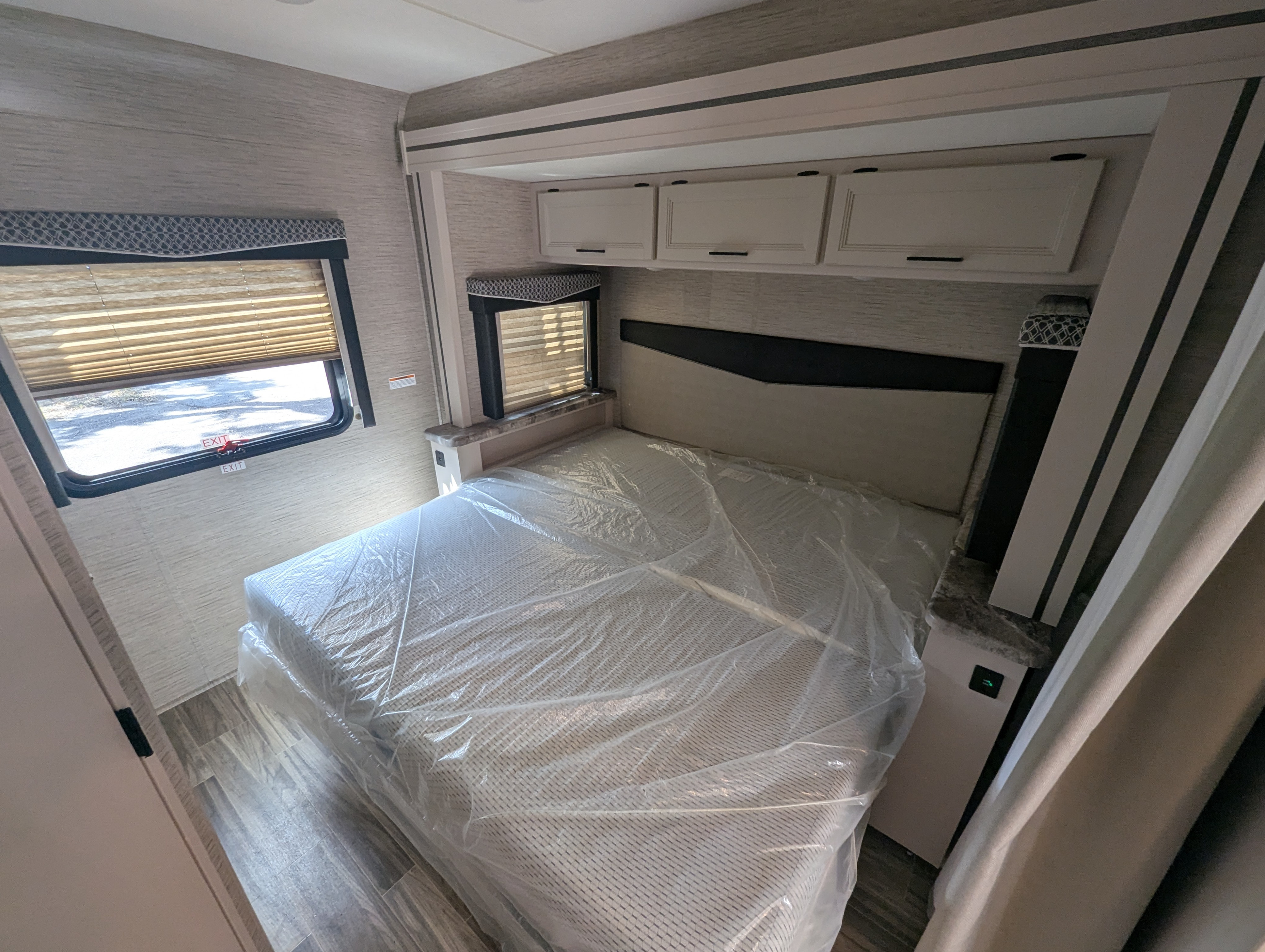 Clean and ready RV rental bedroom featuring a plastic-covered bed, windows, and overhead storage for comfortable travel.. Thor A.C.E. 2022