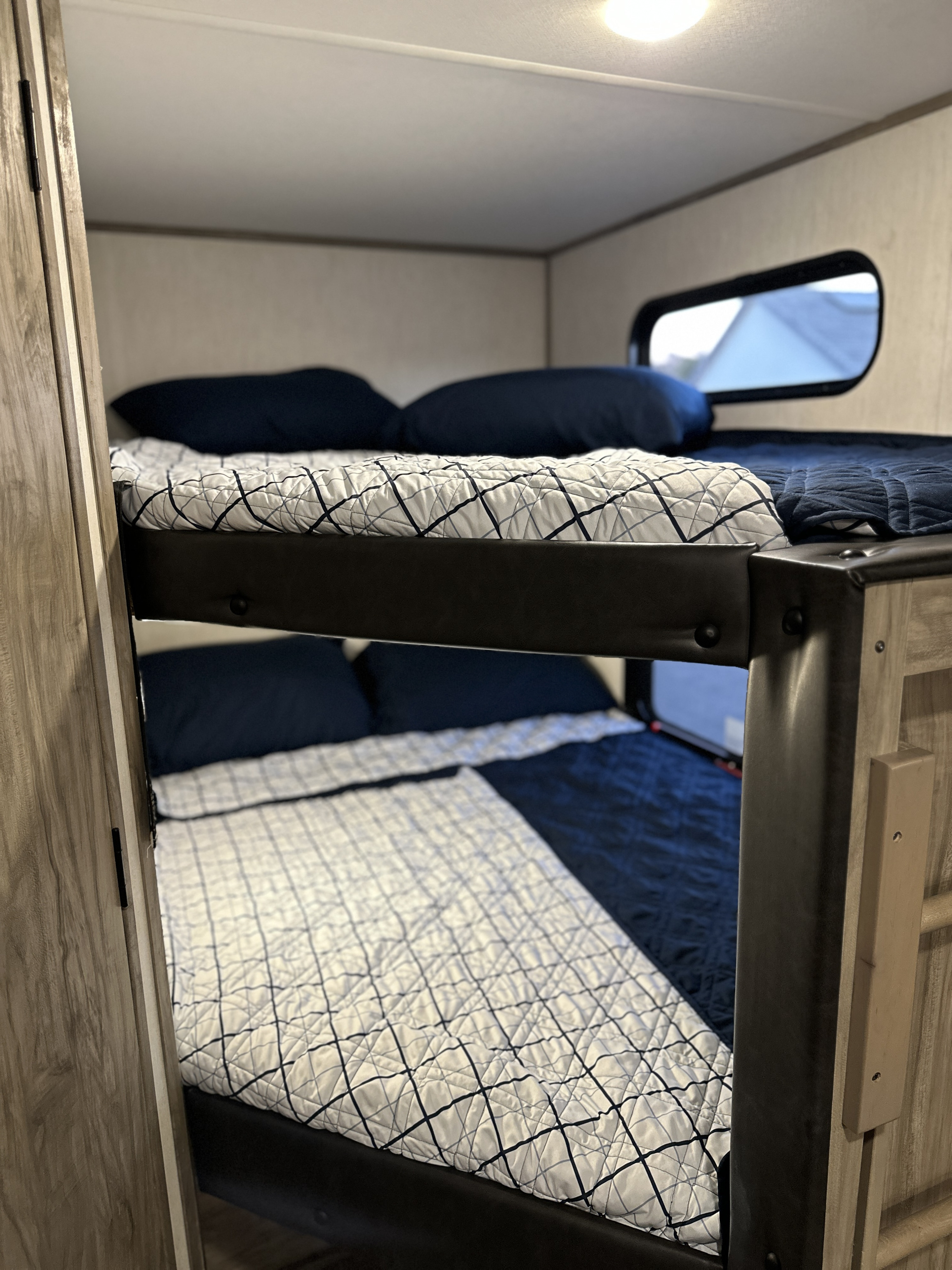 RV rental features cozy bunk beds. The upper bed has a white patterned quilt; the lower, navy. Ideal for family travel.. Forest River Cherokee Alpha Wolf 2022