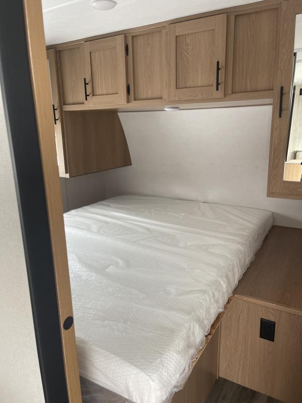 RV rental bedroom features a clean, plastic-wrapped mattress, overhead cabinets, and bedside storage.. Prime Time Avenger 2022