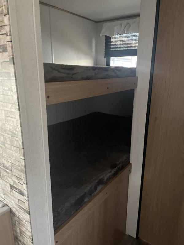 This rv rental features built-in bunk beds with dark mattresses, providing a compact sleeping area inside a travel trailer.. Prime Time Avenger 2022