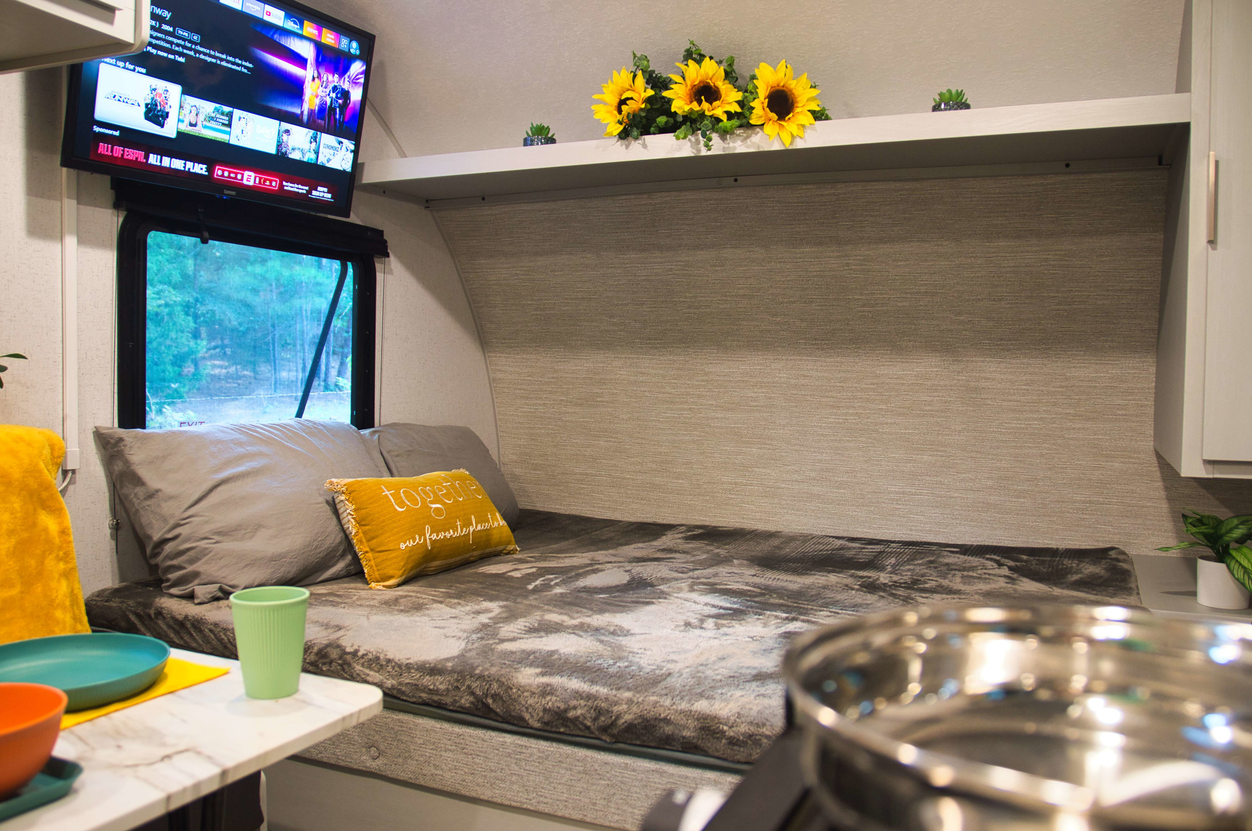 RV rental: Cozy camper bed with TV, a window view of trees, and bright decor on a shelf.. Forest river Salem FSX 2023