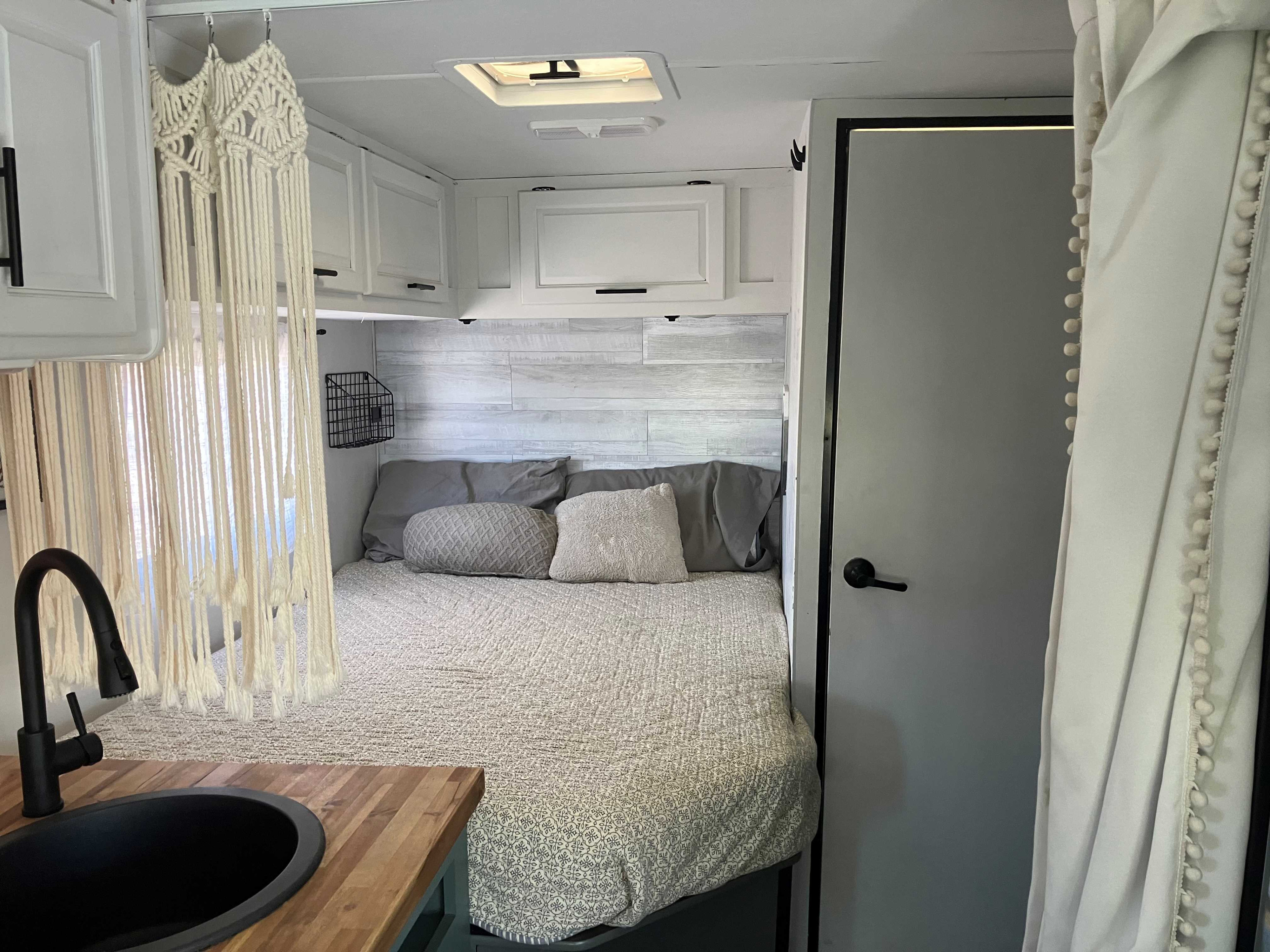 RV rental bedroom & kitchen sink area with modern white cabinets and stylish macrame decor for a cozy interior.. Thor Majestic 2018