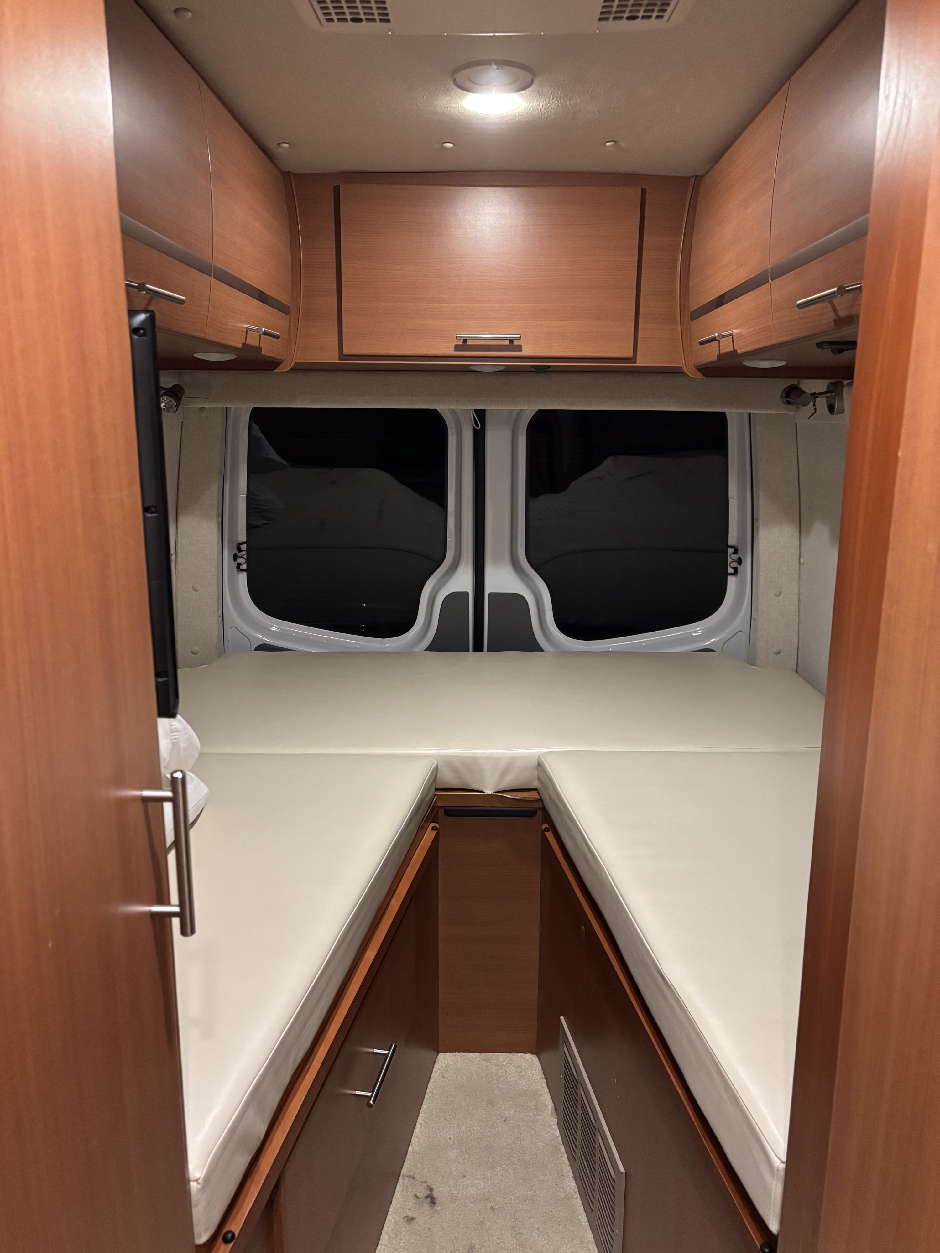 Inside an RV rental: Looking towards the rear, this camper van features twin beds, wood cabinets, and dark rear windows.. Winnebago Era 170A 2013