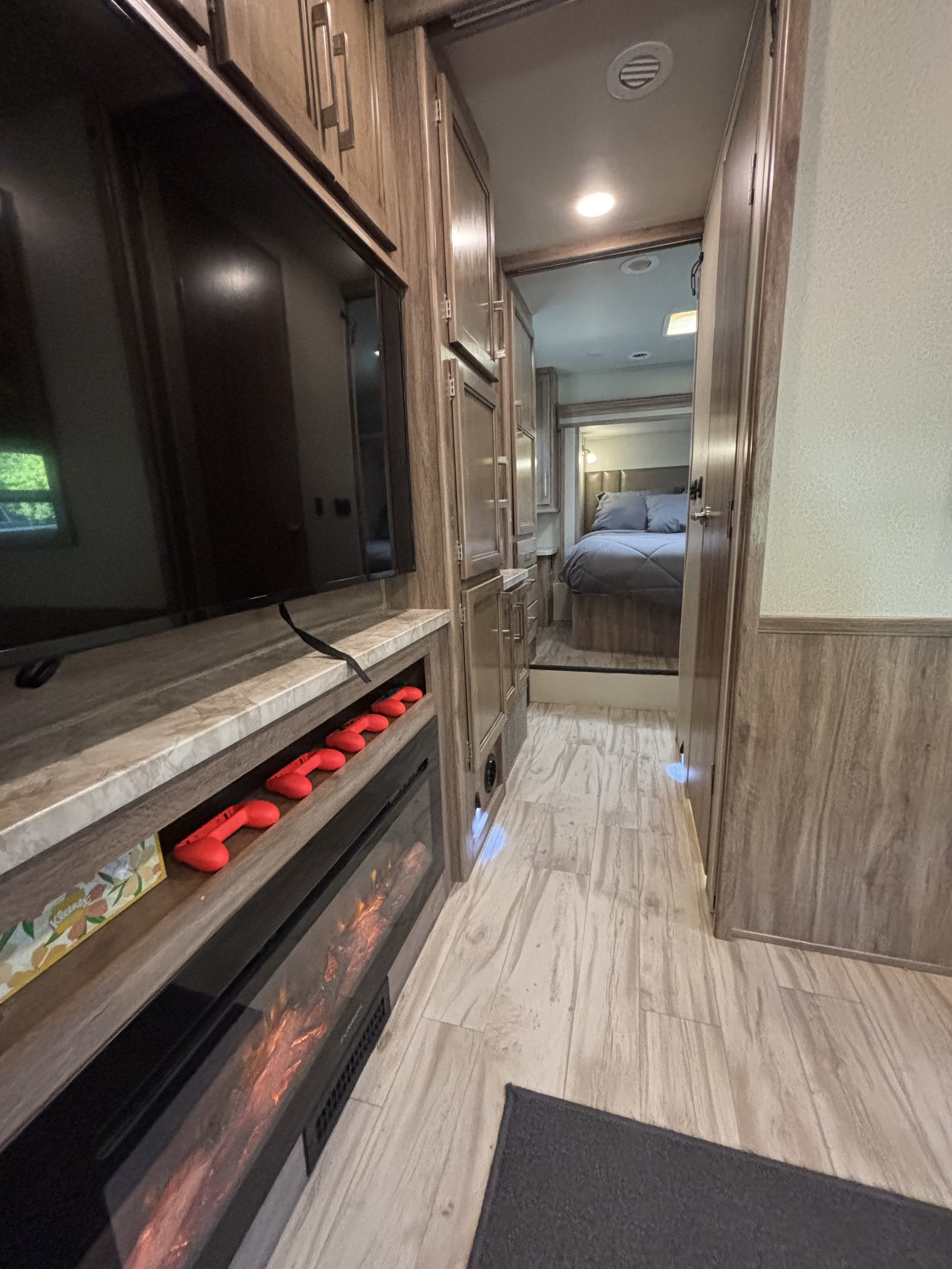 Inside a cozy RV rental: living area with TV, red controllers, and fireplace, leading to a comfortable bedroom.. Entegra Coach Odyssey 2019