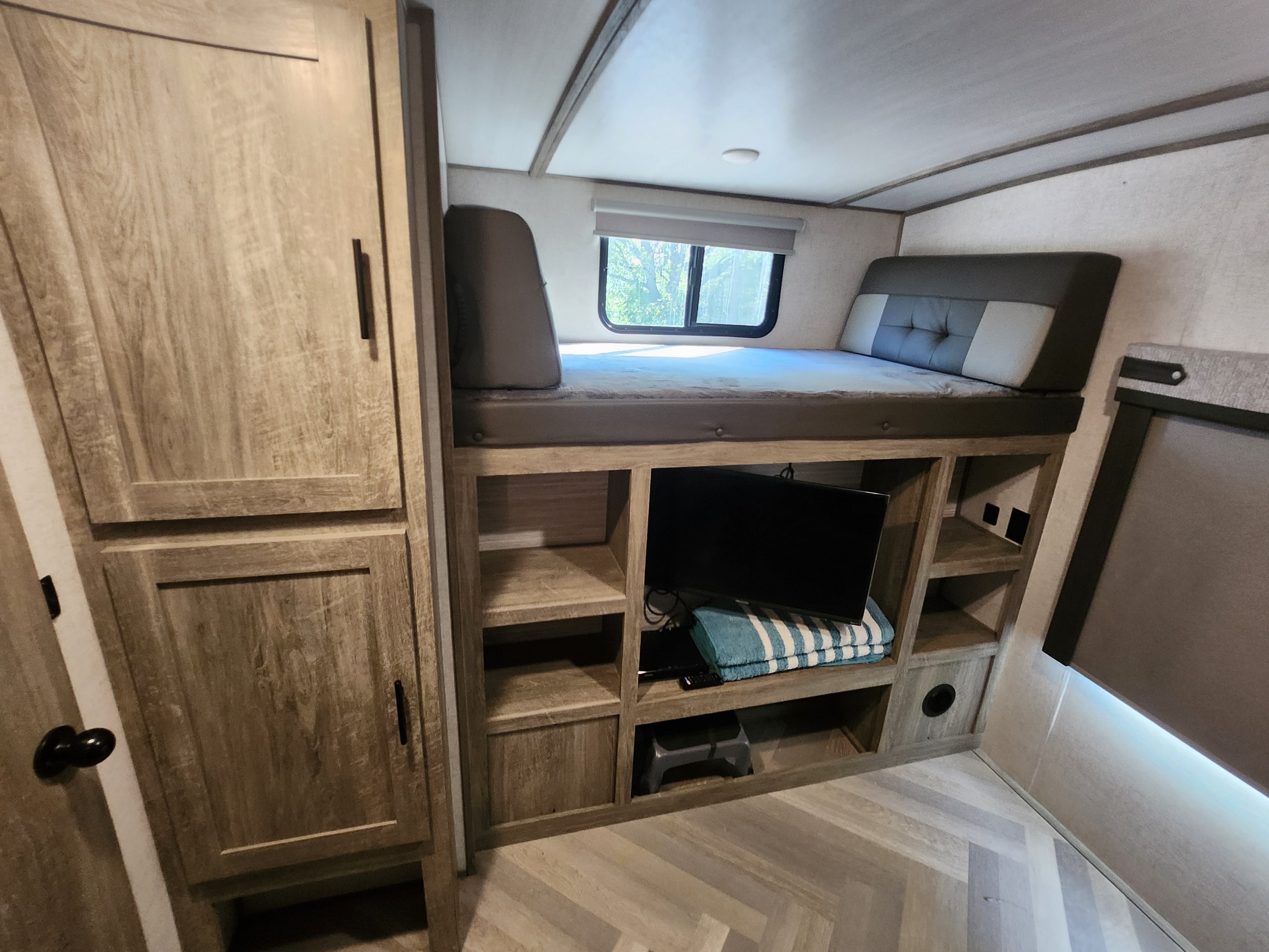 RV rental bunk bed with integrated TV and shelving unit, plus a wardrobe, providing practical sleeping and storage.. Forest River Wildwood Heritage Glen 2021